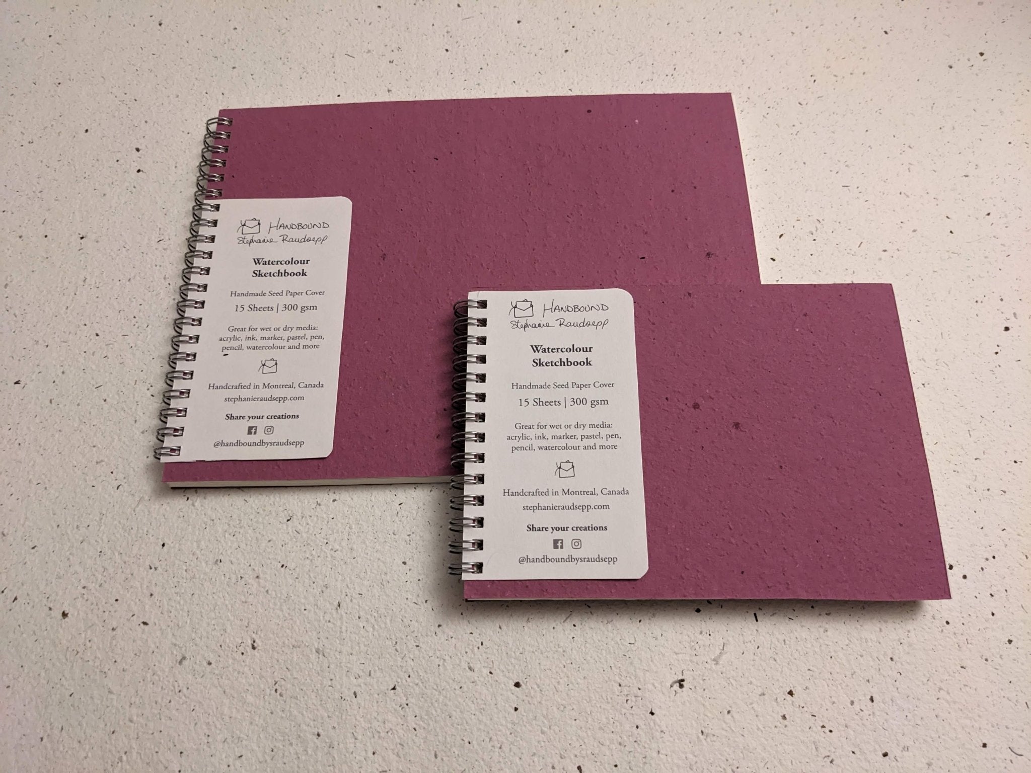 Two purple notebooks with white labels on a speckled surface Large Plantable Watercolour Sketchbook by Creative Artifacts HQ