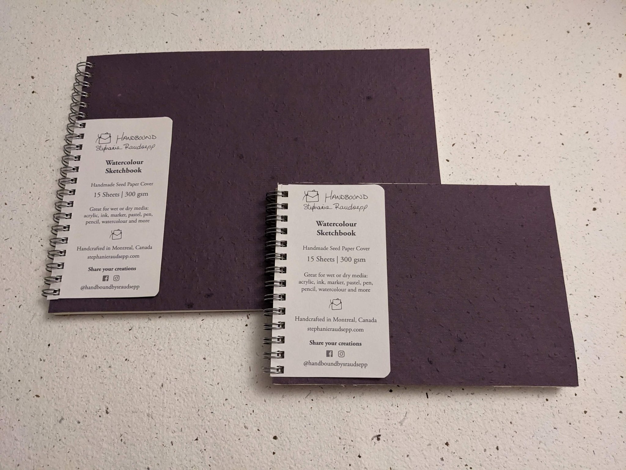 Two purple notebooks with white labels on a textured surface Plantable Watercolour Sketchbook by Creative Artifacts HQ