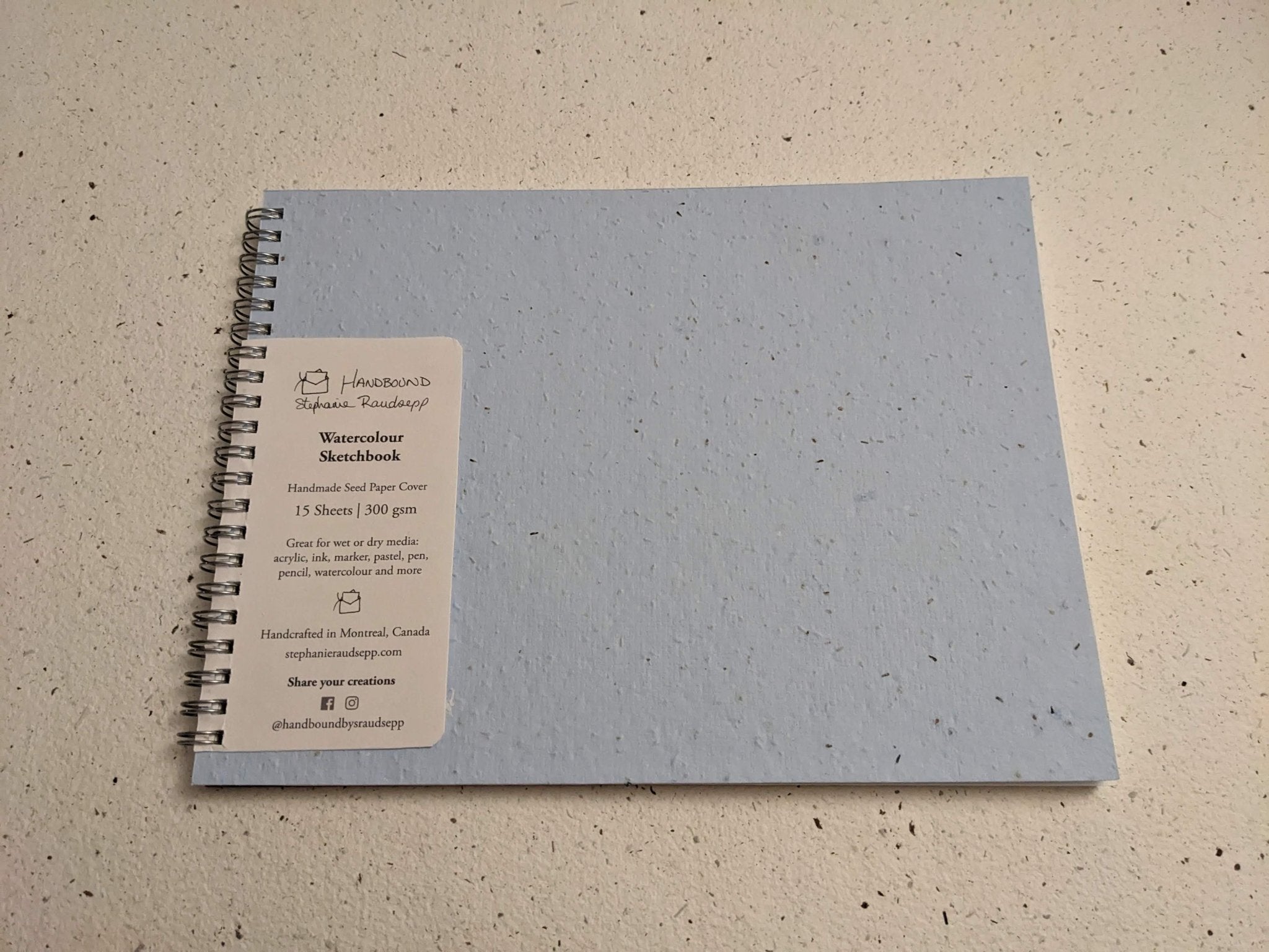 Gray spiral-bound notebook on a beige textured surface Plantable Watercolour Sketchbook by Creative Artifacts HQ