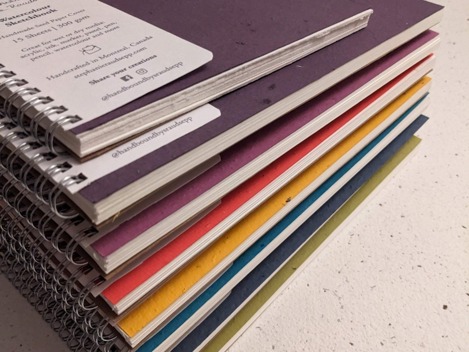 Stack of colorful notebooks on a textured surface Large Plantable Watercolour Sketchbook by Creative Artifacts HQ
