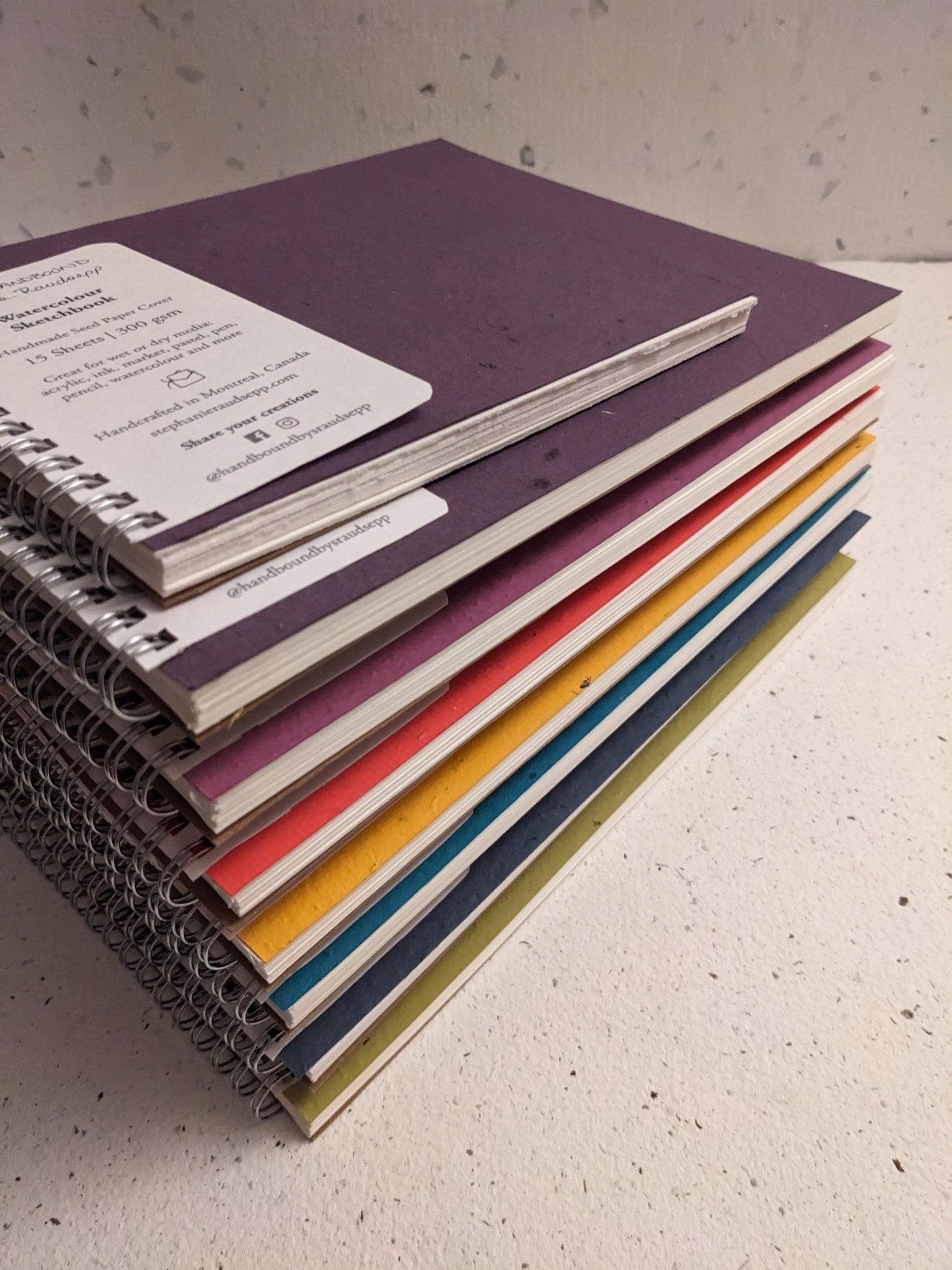 Stack of colorful notebooks on a textured surface Plantable Watercolour Sketchbook by Creative Artifacts HQ