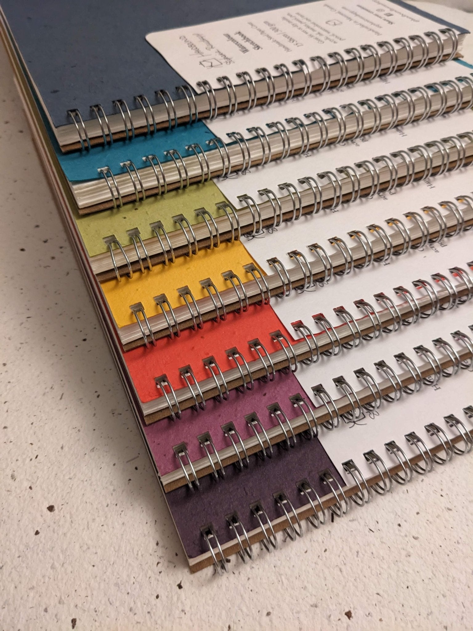 Colorful spiral-bound notebooks stacked on a textured surface Plantable Watercolour Sketchbook by Creative Artifacts HQ