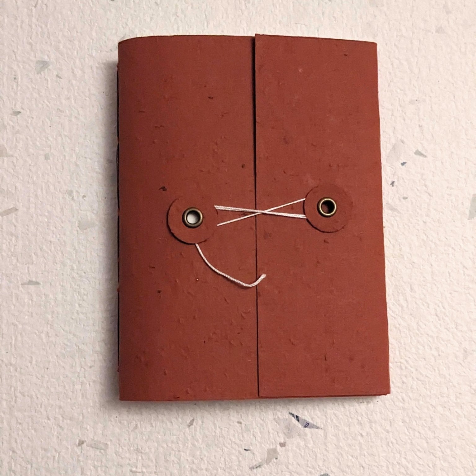 Brown hand stitched plantable paper notebook with string closure on a light grey background Creative Artifacts HQ