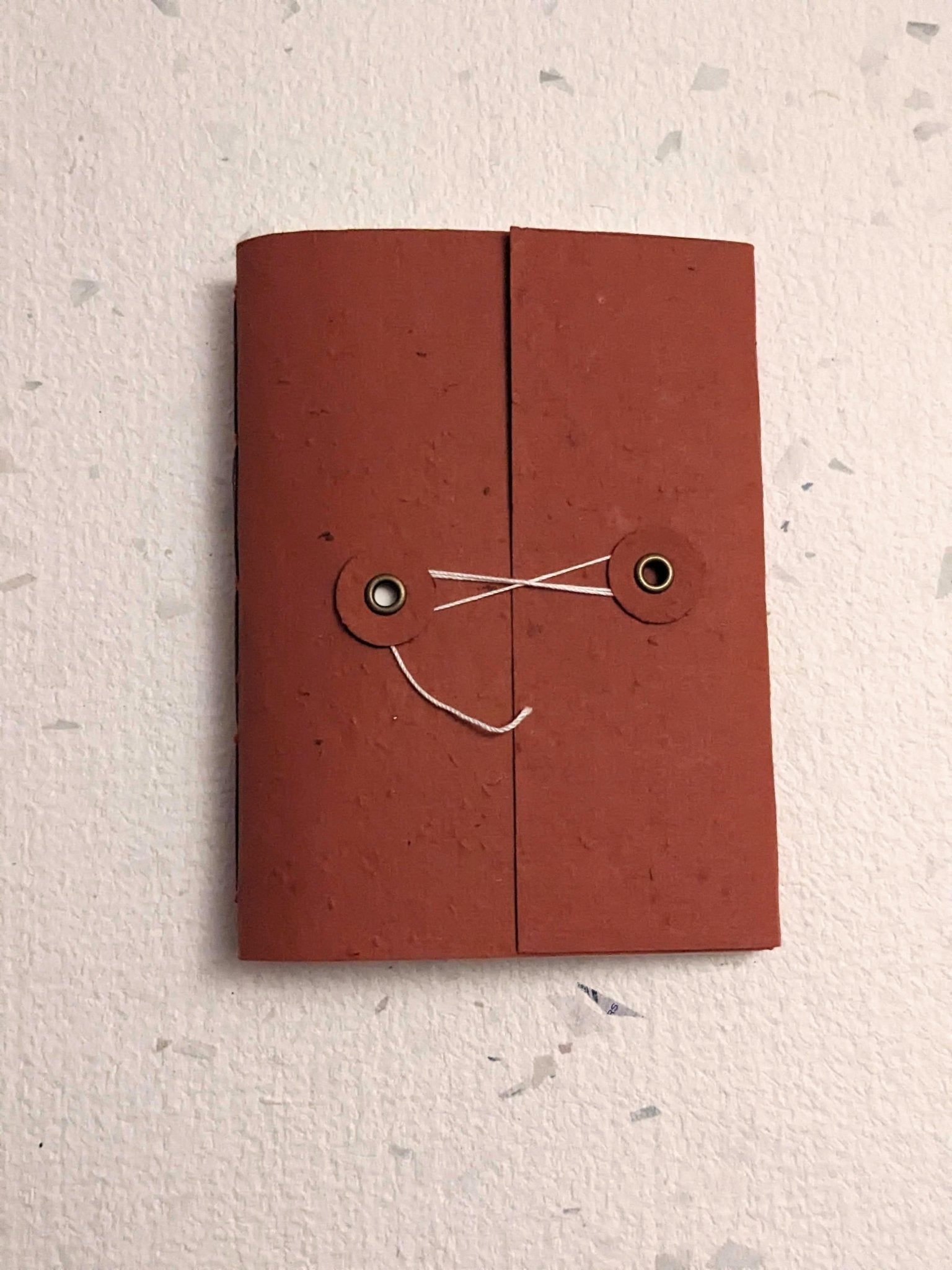 Brown hand stitched plantable paper notebook with string closure on a light grey background Creative Artifacts HQ