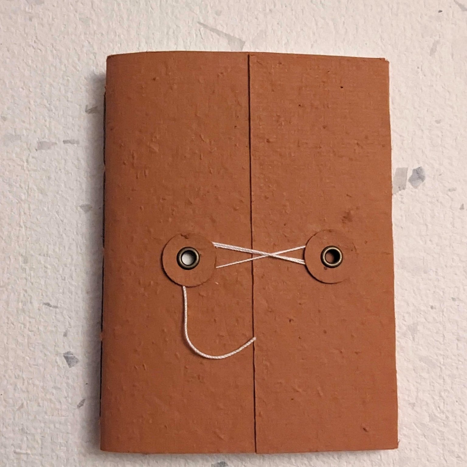 Brown hand stitched plantable paper notebook with string closure on a light grey background Creative Artifacts HQ