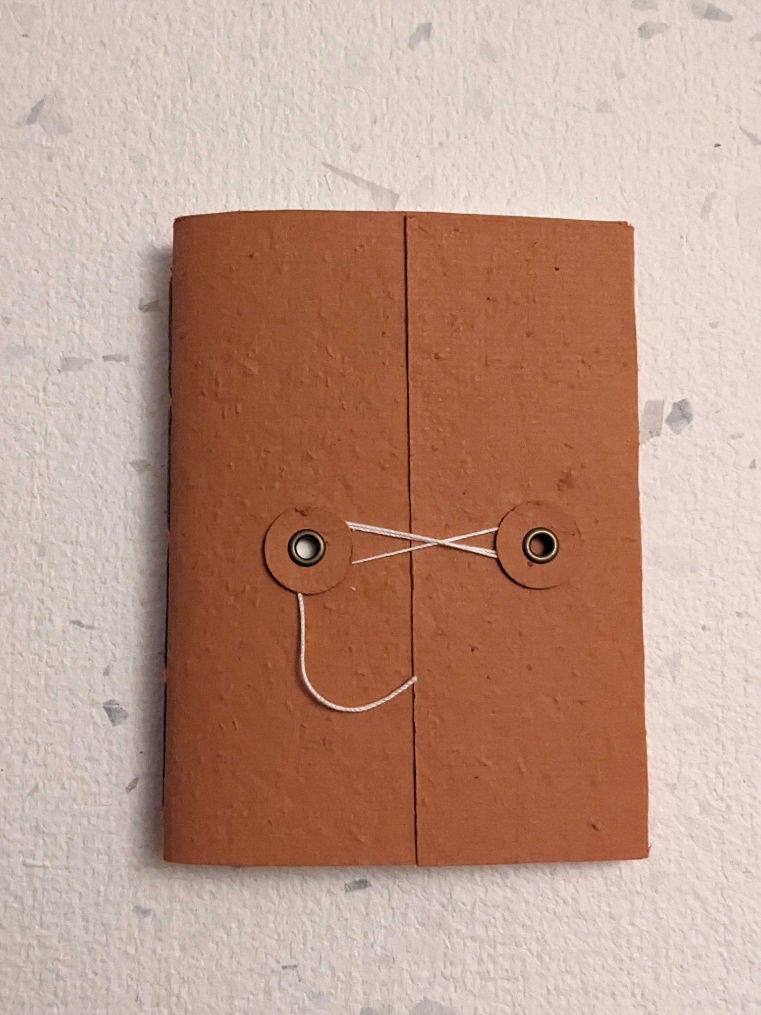 Brown hand stitched plantable paper notebook with string closure on a light grey background Creative Artifacts HQ
