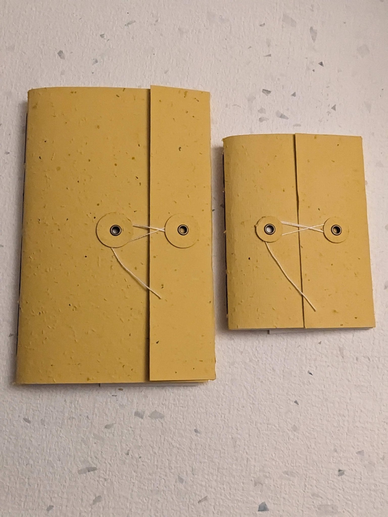 Two yellow notebooks with string ties on a textured grey surface Creative Artifacts HQ plantable 