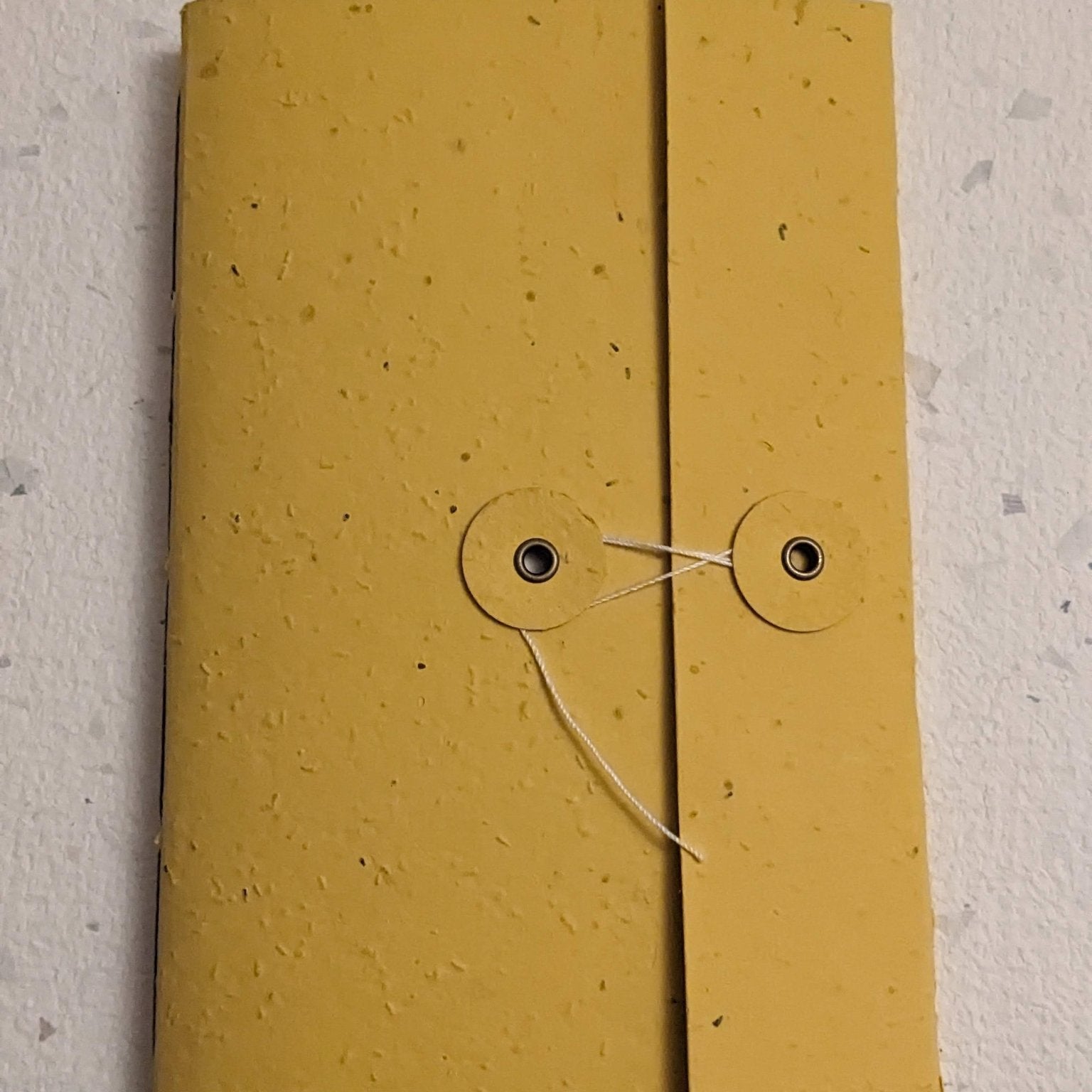 Yellow notebook with a string closure on a light grey background Creative Artifacts HQ plantable 