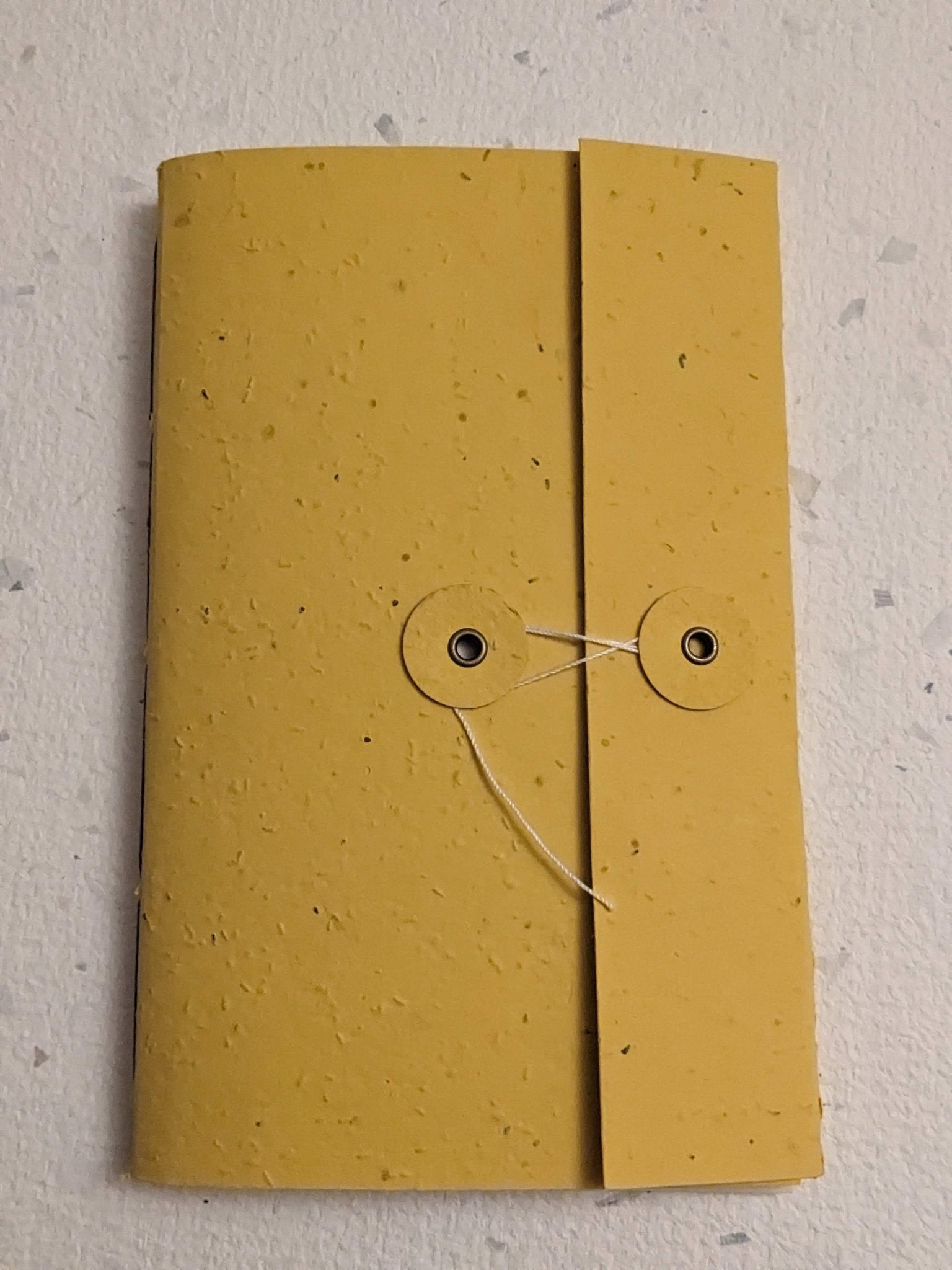Yellow notebook with a string closure on a light grey background Creative Artifacts HQ plantable 
