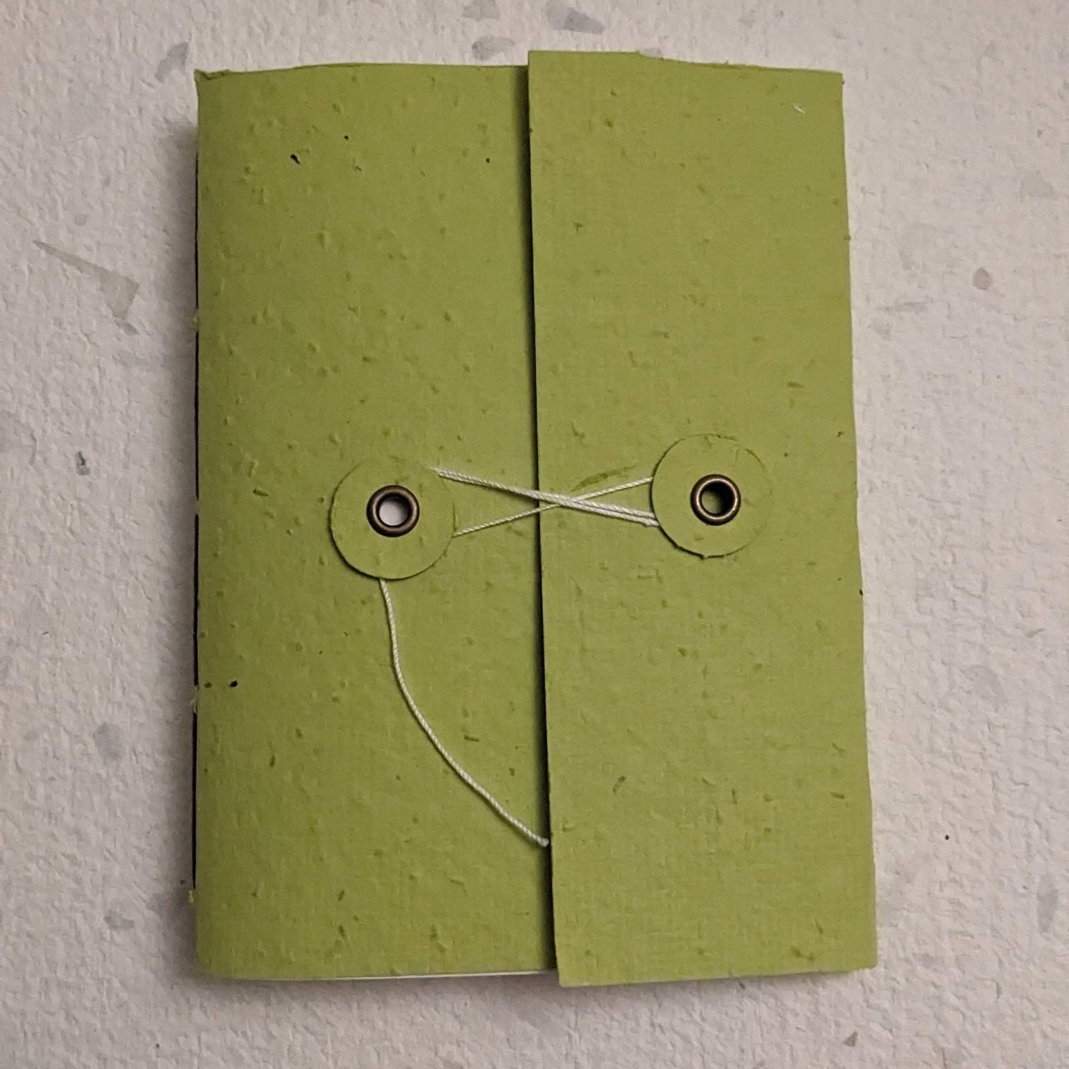 Green paper hand stitched plantable paper notebook with string closure on a light grey background Creative Artifacts HQ