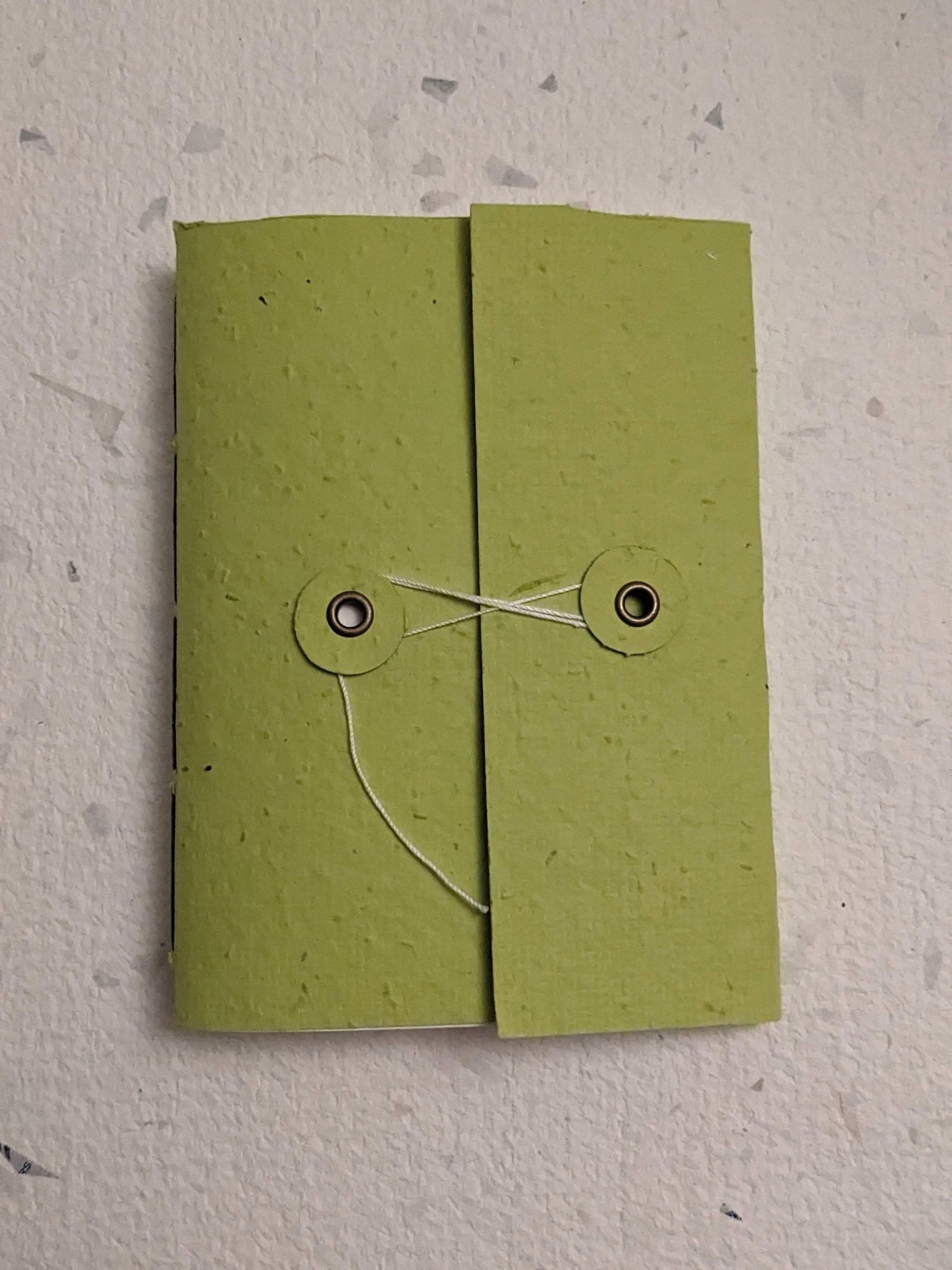 Green paper hand stitched plantable paper notebook with string closure on a light grey background Creative Artifacts HQ
