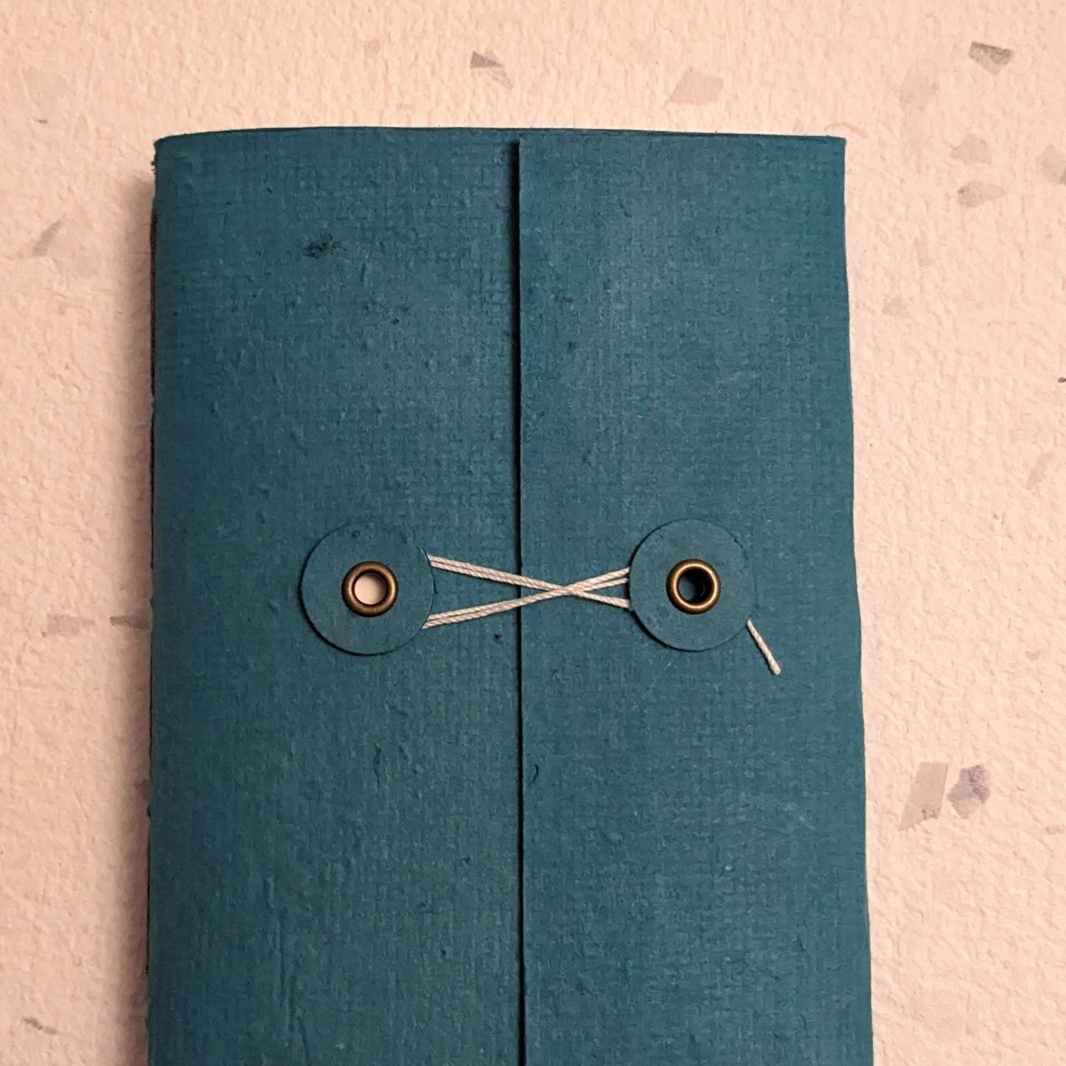 Blue fabric book with button closure hand stitched plantable paper notebook with string closure on a light grey background Creative Artifacts HQ