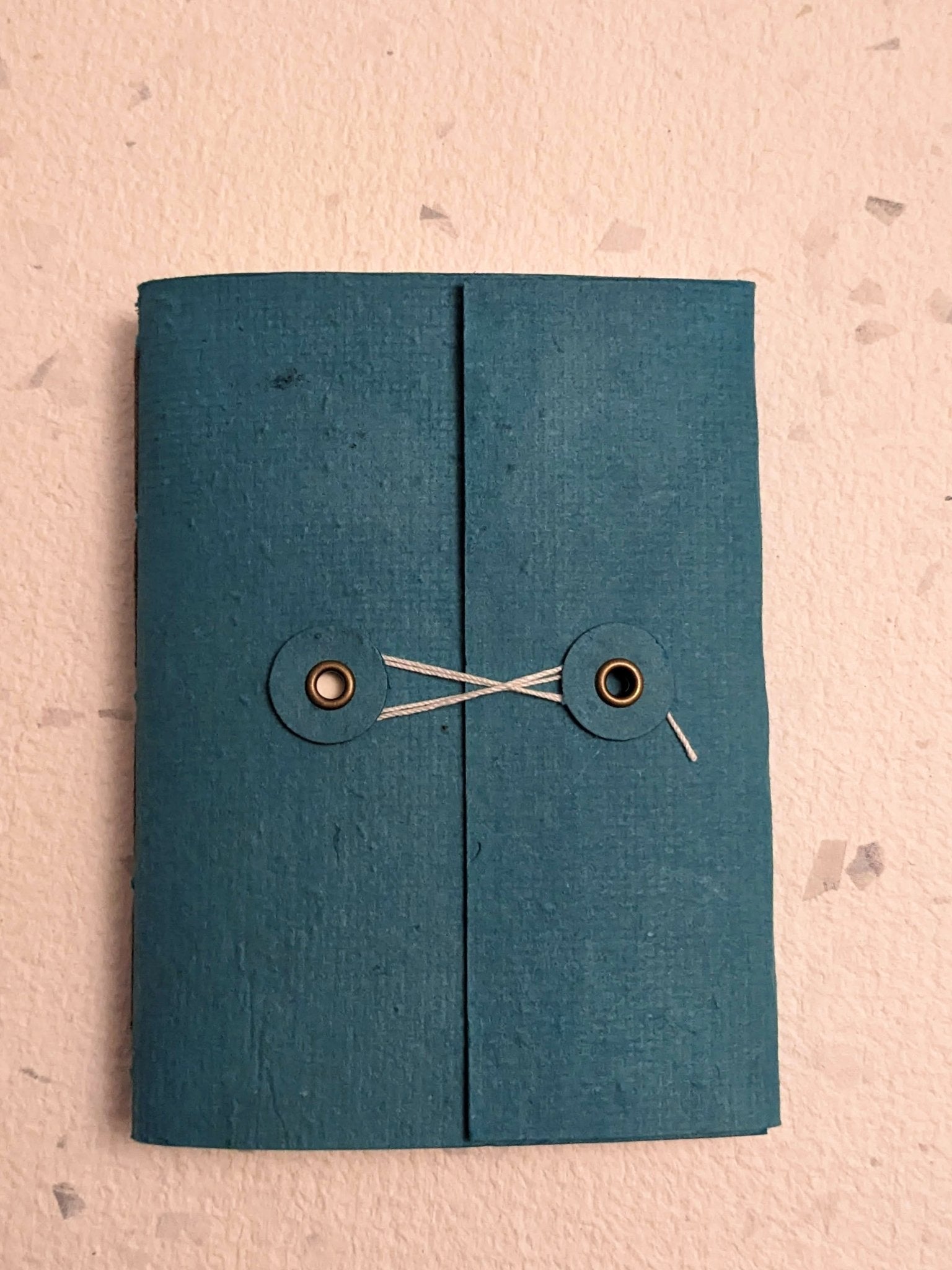 Blue fabric book with button closure hand stitched plantable paper notebook with string closure on a light grey background Creative Artifacts HQ