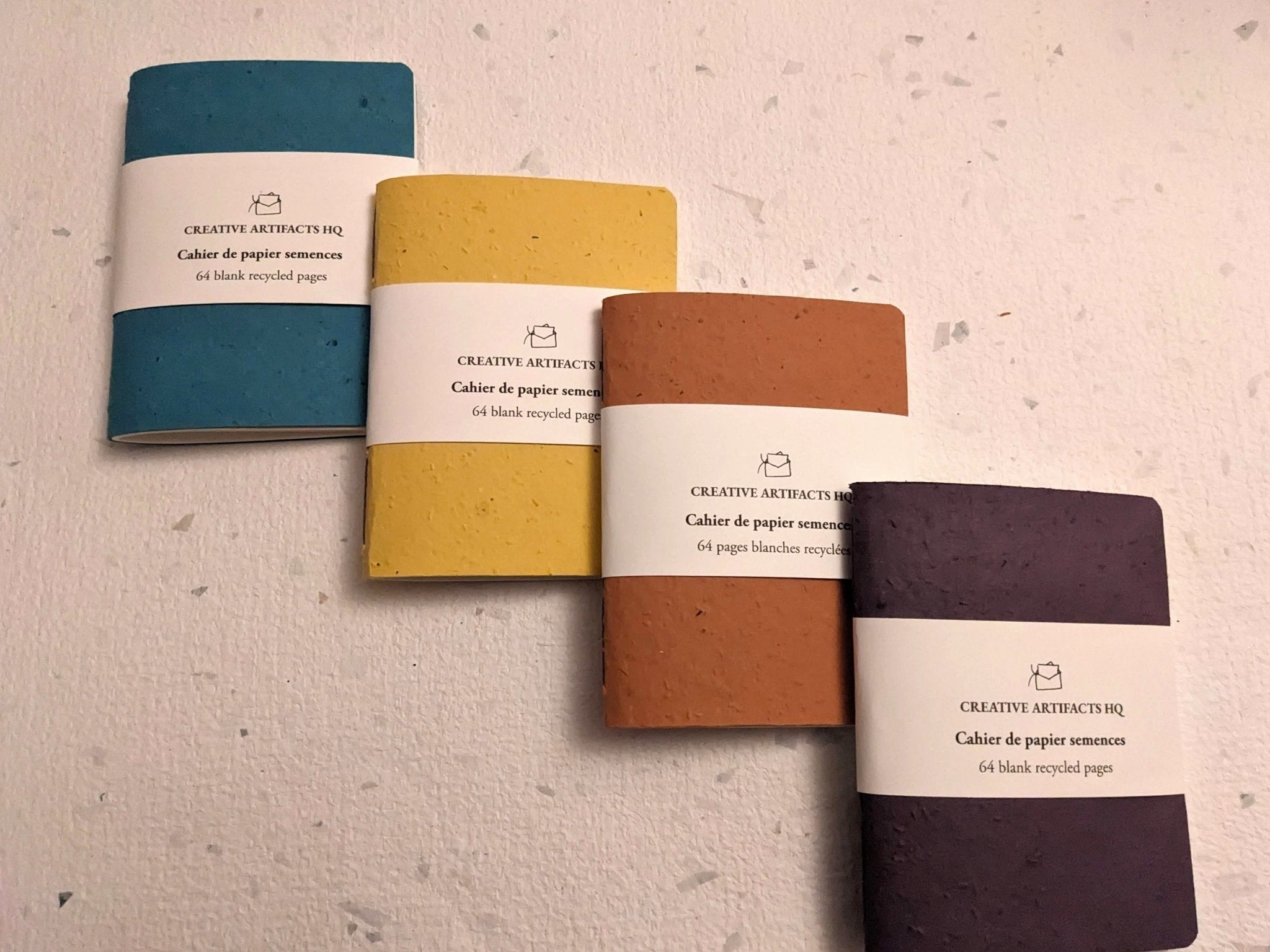 Four notebooks in different colors on a hand stitched plantable paper notebook on a light grey background Creative Artifacts HQ