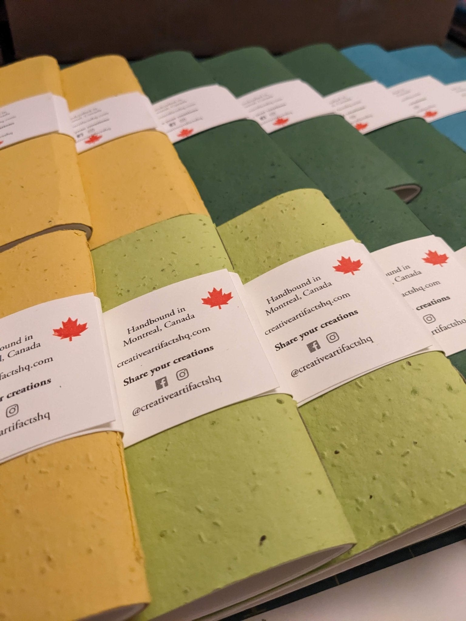 Row of small notebooks with visible brand labels on a hand stitched plantable paper notebook on a light grey background Creative Artifacts HQ