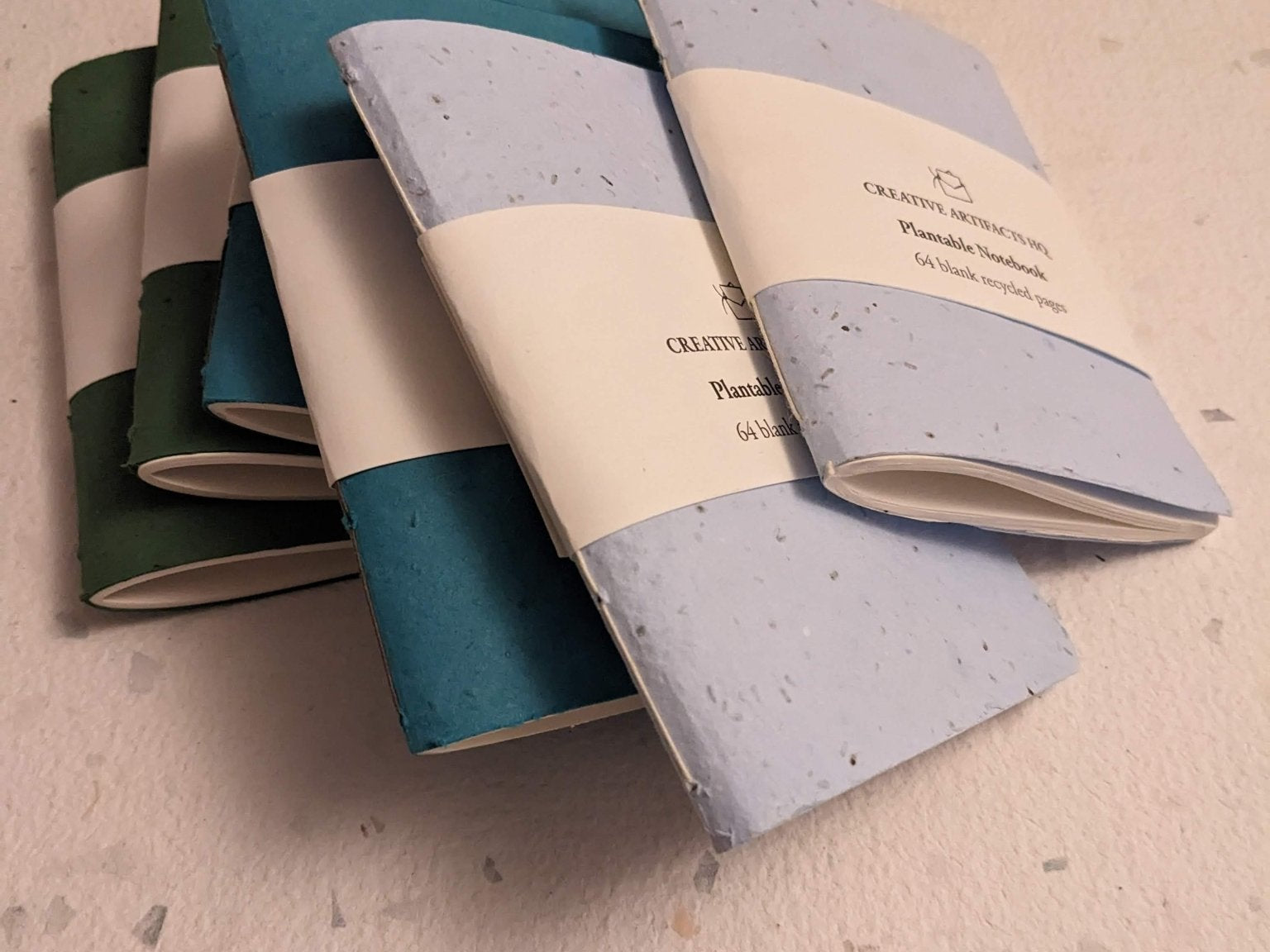 Set of three notebooks with different color combinations on a hand stitched plantable paper notebook on a light grey background Creative Artifacts HQ
