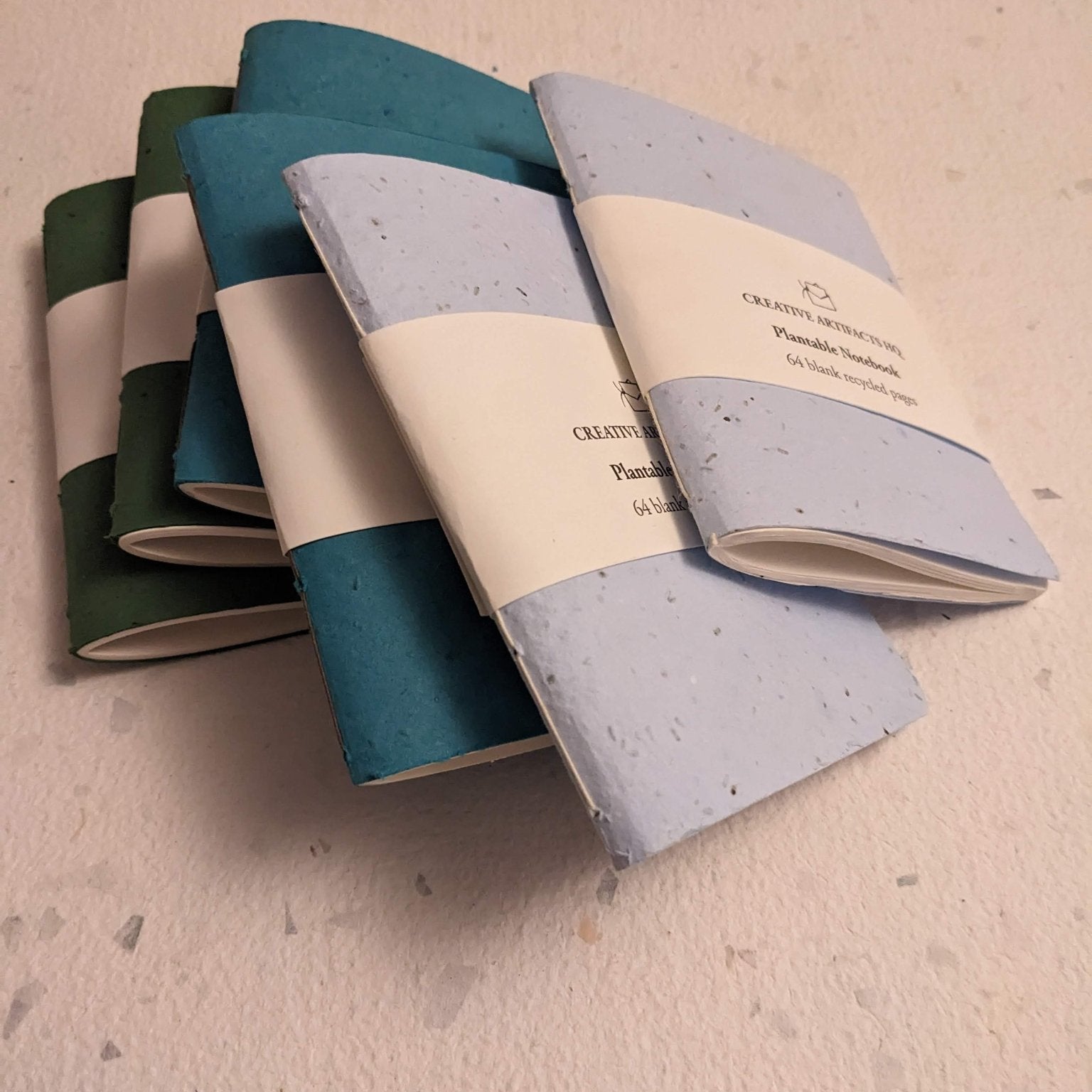 Set of three notebooks with different color combinations on a hand stitched plantable paper notebook on a light grey background Creative Artifacts HQ