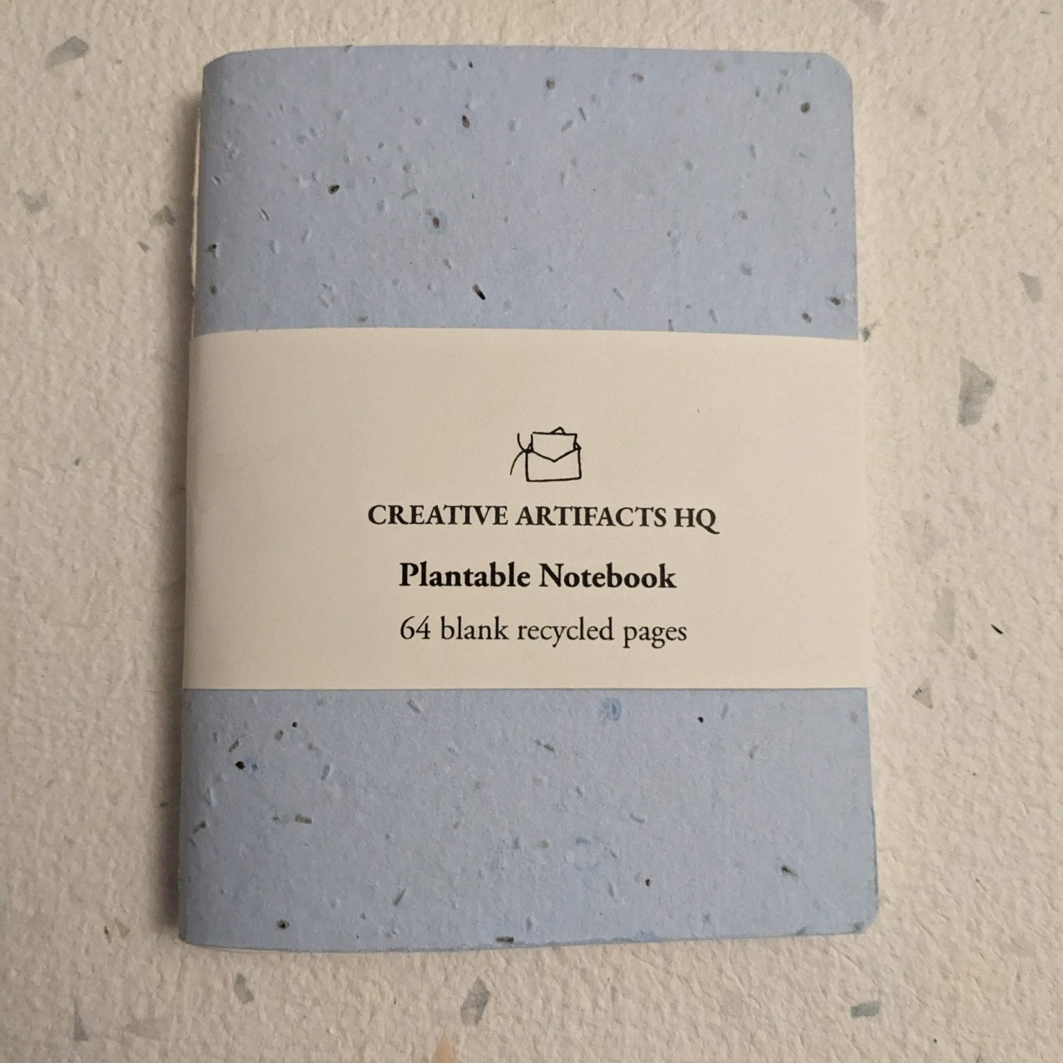 Plantable notebook with light blue cover and a hand stitched plantable paper notebook on a light grey background Creative Artifacts HQ
