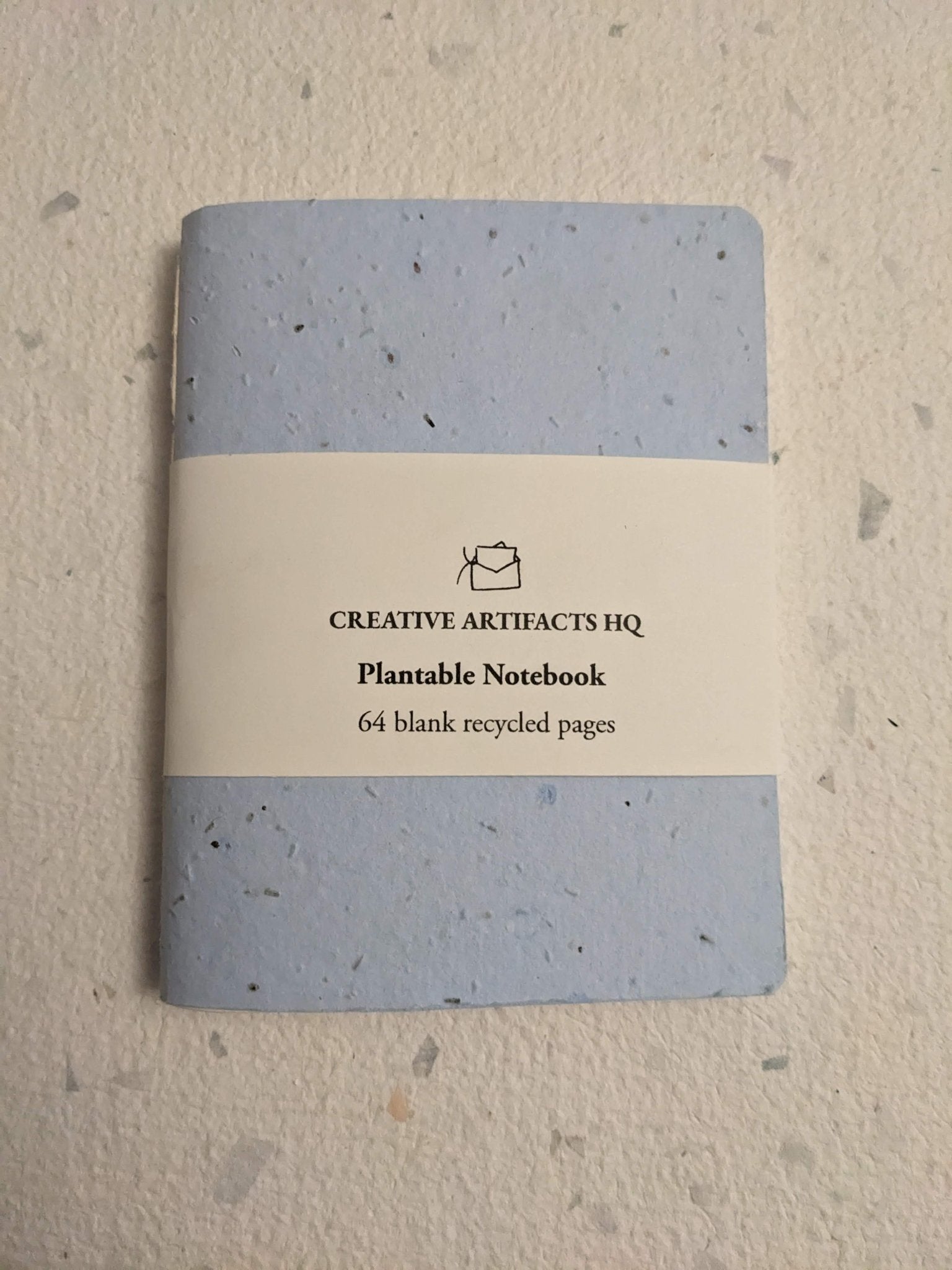 Plantable notebook with light blue cover and a hand stitched plantable paper notebook on a light grey background Creative Artifacts HQ
