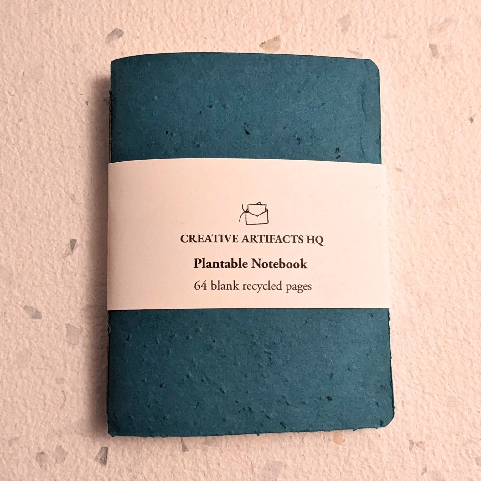 Teal notebook with a label on a hand stitched plantable paper notebook on a light grey background Creative Artifacts HQ