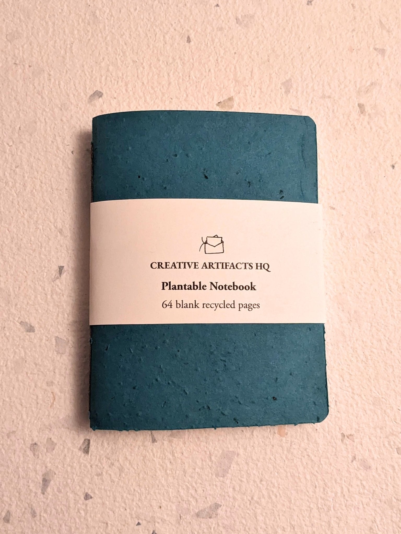 Teal notebook with a label on a hand stitched plantable paper notebook on a light grey background Creative Artifacts HQ