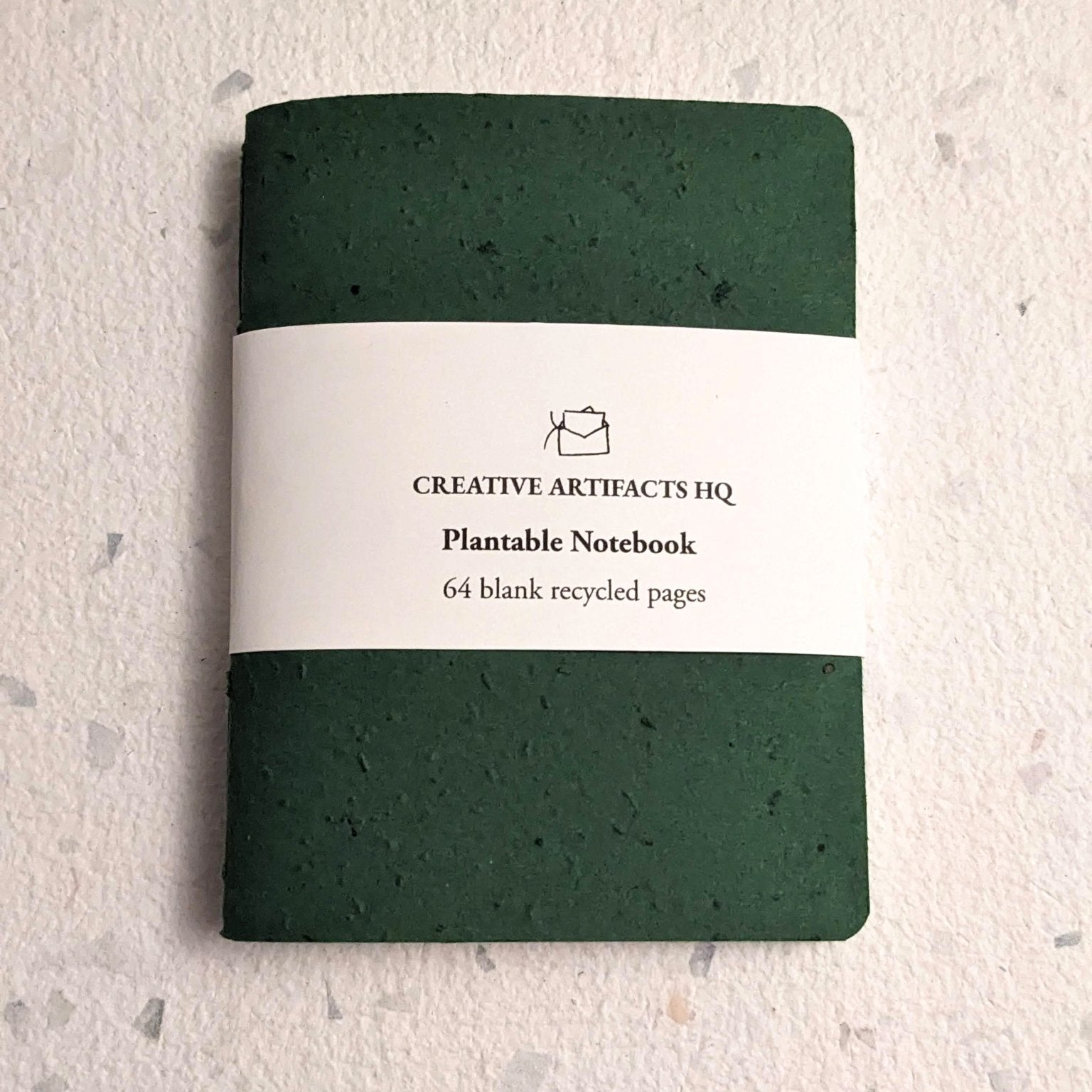 Green plantable notebook with a visible brand label on a textured hand stitched plantable paper notebook with string closure on a light grey background Creative Artifacts HQ