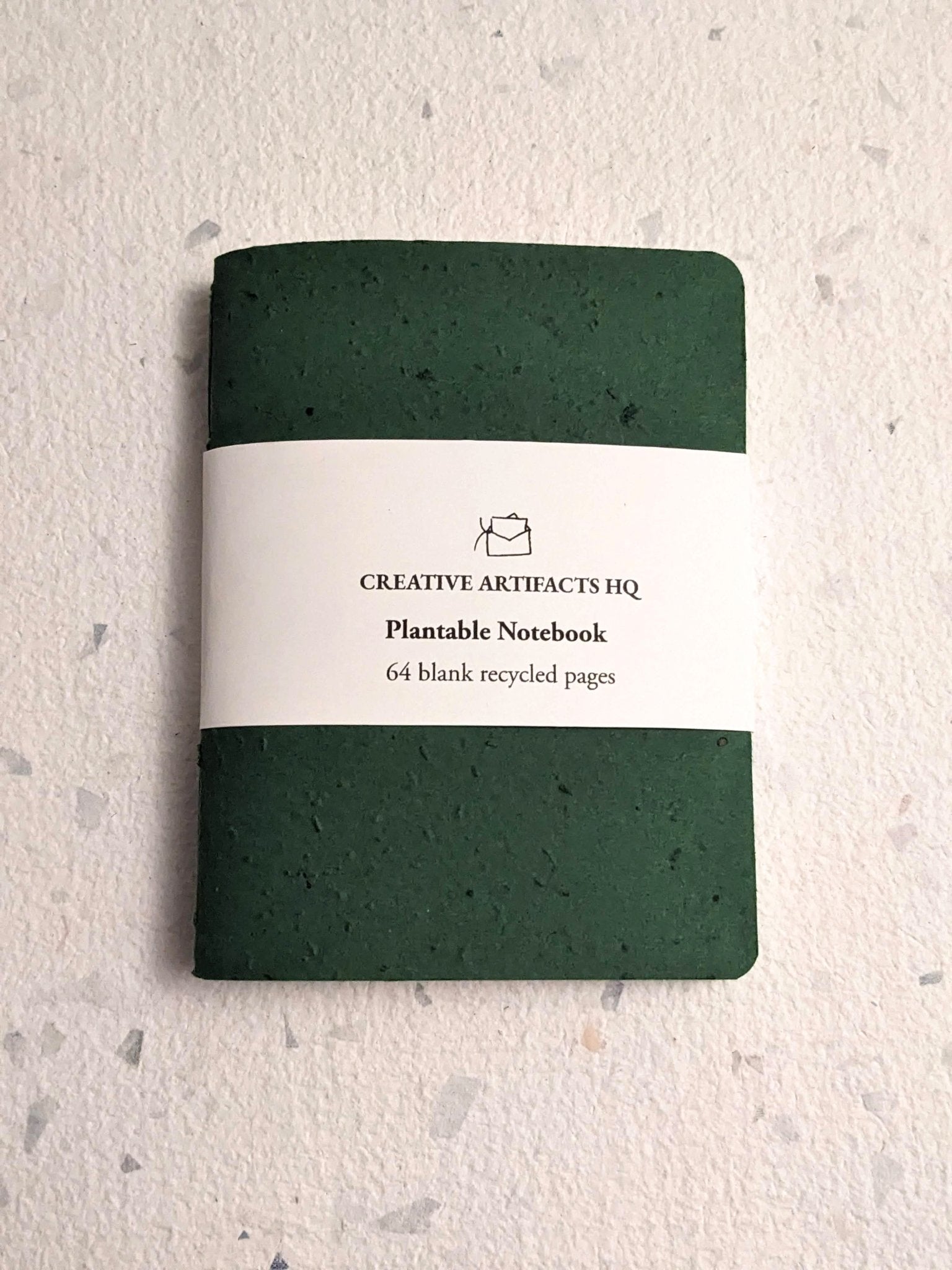 Green plantable notebook with a visible brand label on a textured hand stitched plantable paper notebook with string closure on a light grey background Creative Artifacts HQ