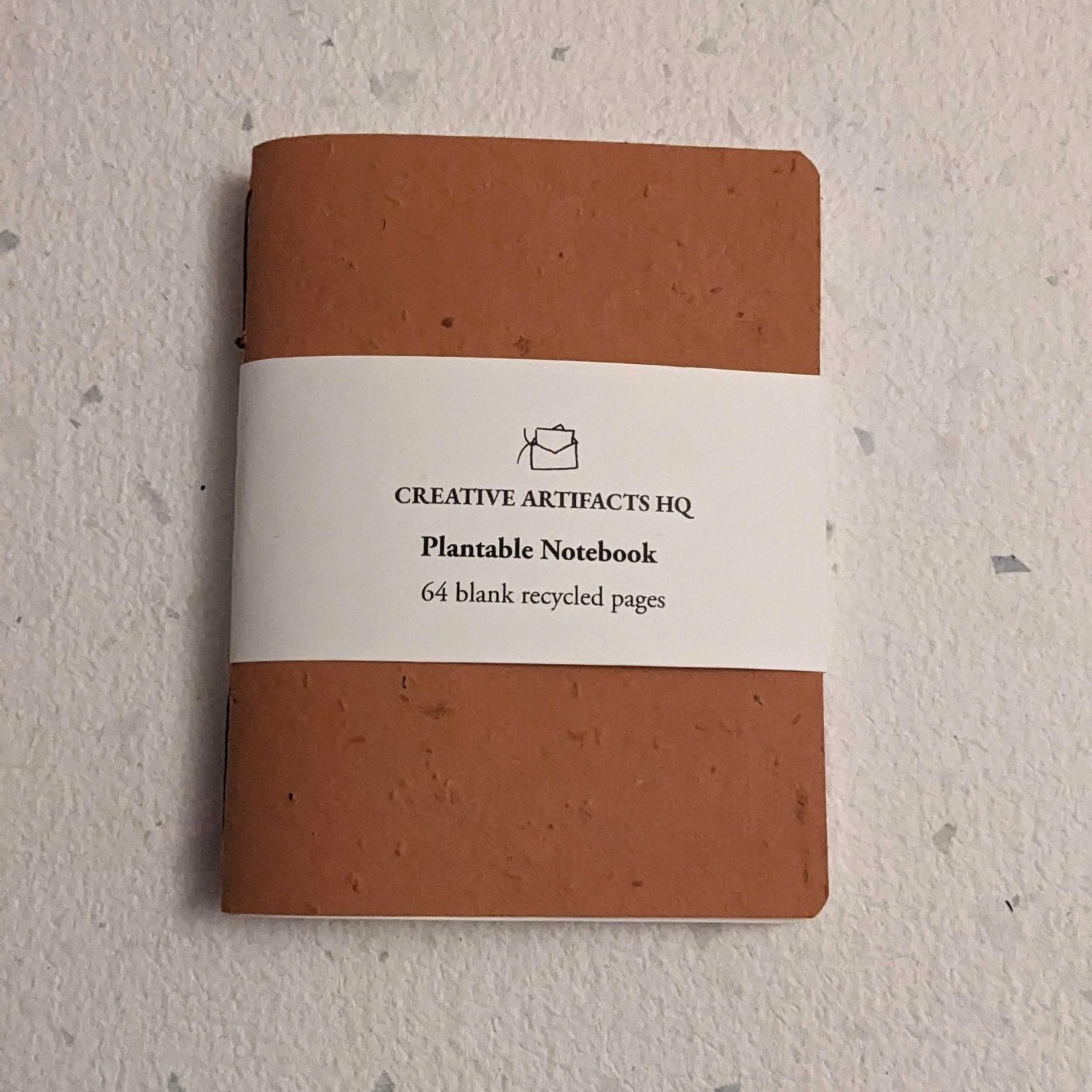 Brown notebook with a white label on a hand stitched plantable paper notebook on a light grey background Creative Artifacts HQ