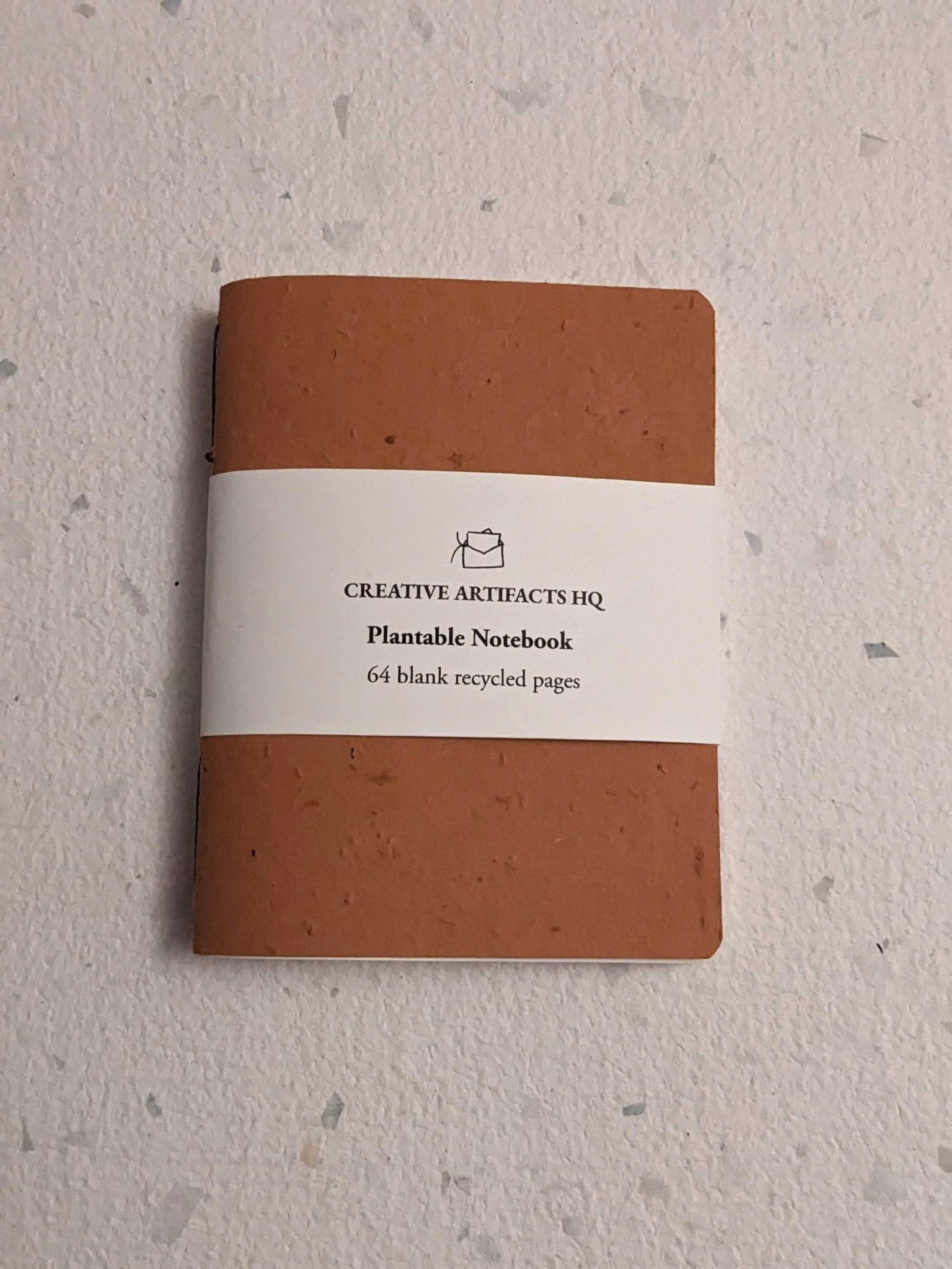 Brown notebook with a white label on a hand stitched plantable paper notebook on a light grey background Creative Artifacts HQ