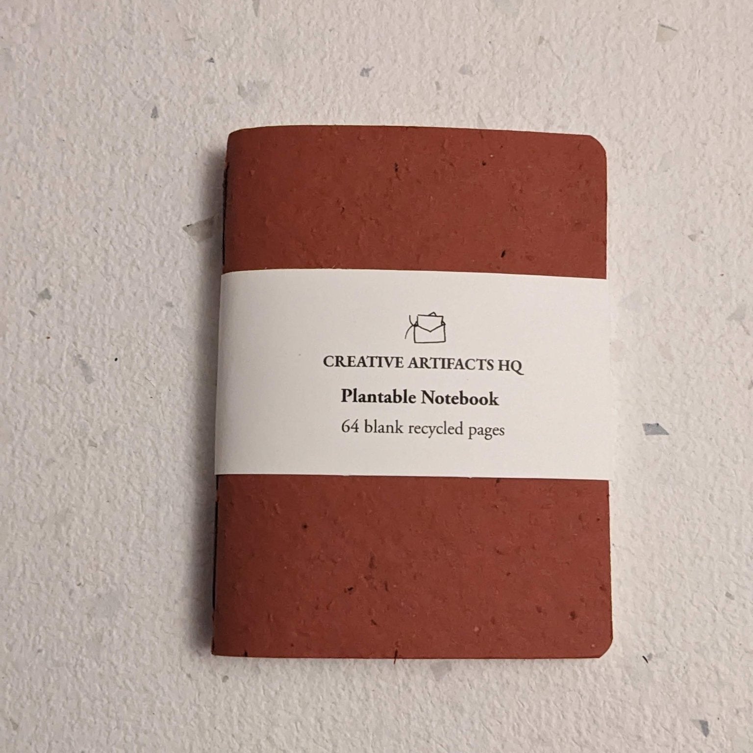 Red notebook with a label on a hand stitched plantable paper notebook on a light grey background Creative Artifacts HQ