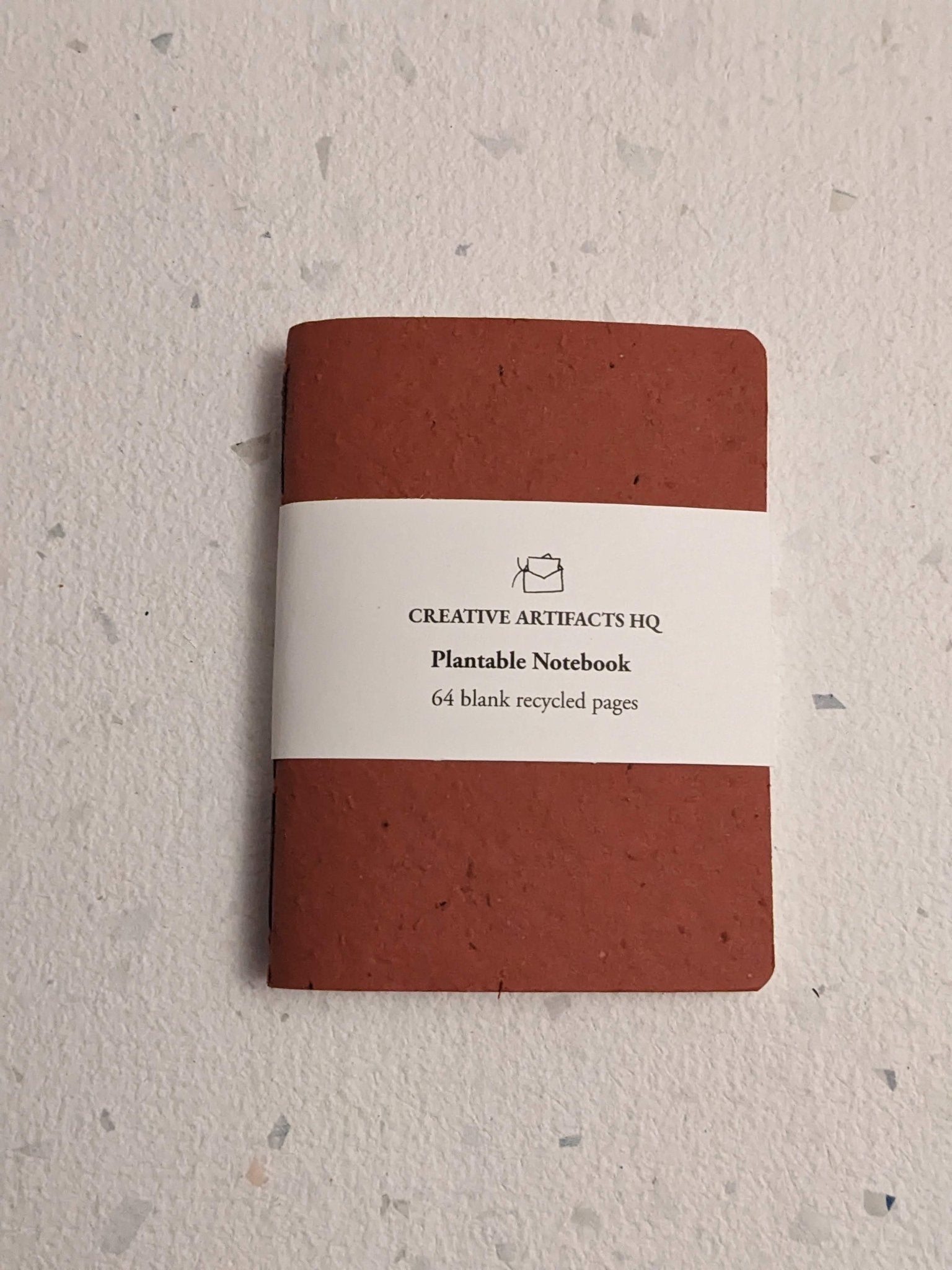 Red notebook with a label on a hand stitched plantable paper notebook on a light grey background Creative Artifacts HQ