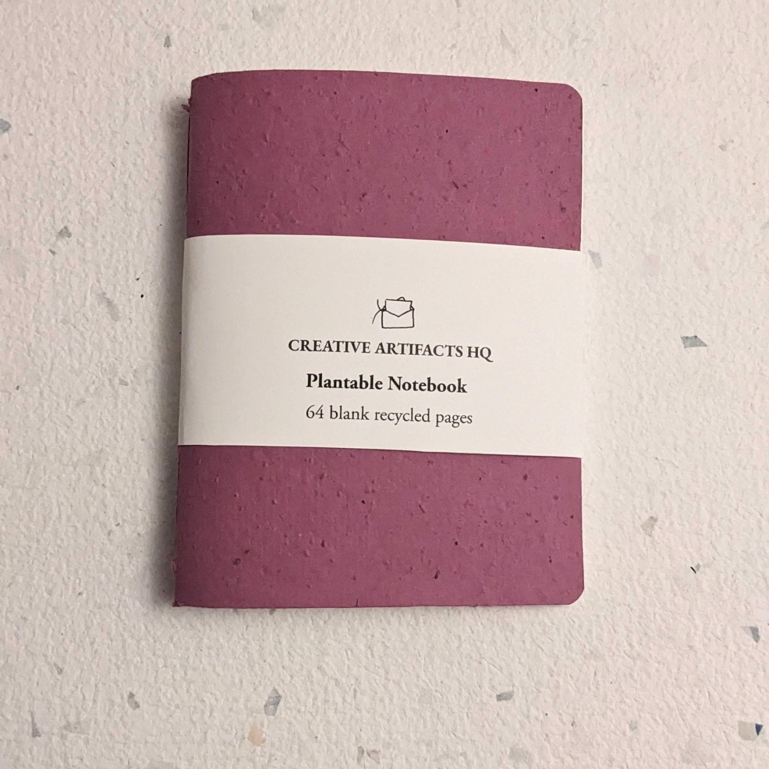 Purple notebook with a white label on  a hand stitched plantable paper notebook on a light grey background Creative Artifacts HQ
