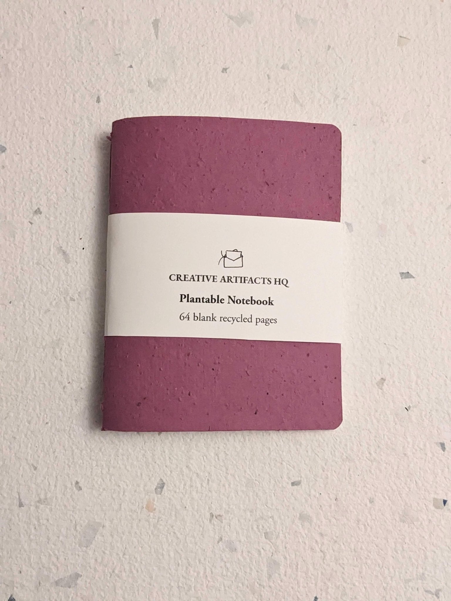 Purple notebook with a white label on  a hand stitched plantable paper notebook on a light grey background Creative Artifacts HQ