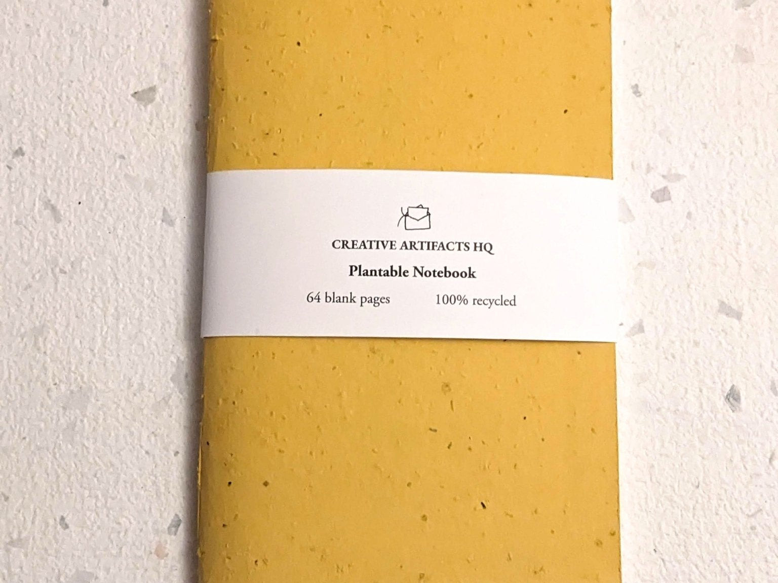 Yellow notebook with a white label on a light grey surface Creative Artifacts HQ plantable 