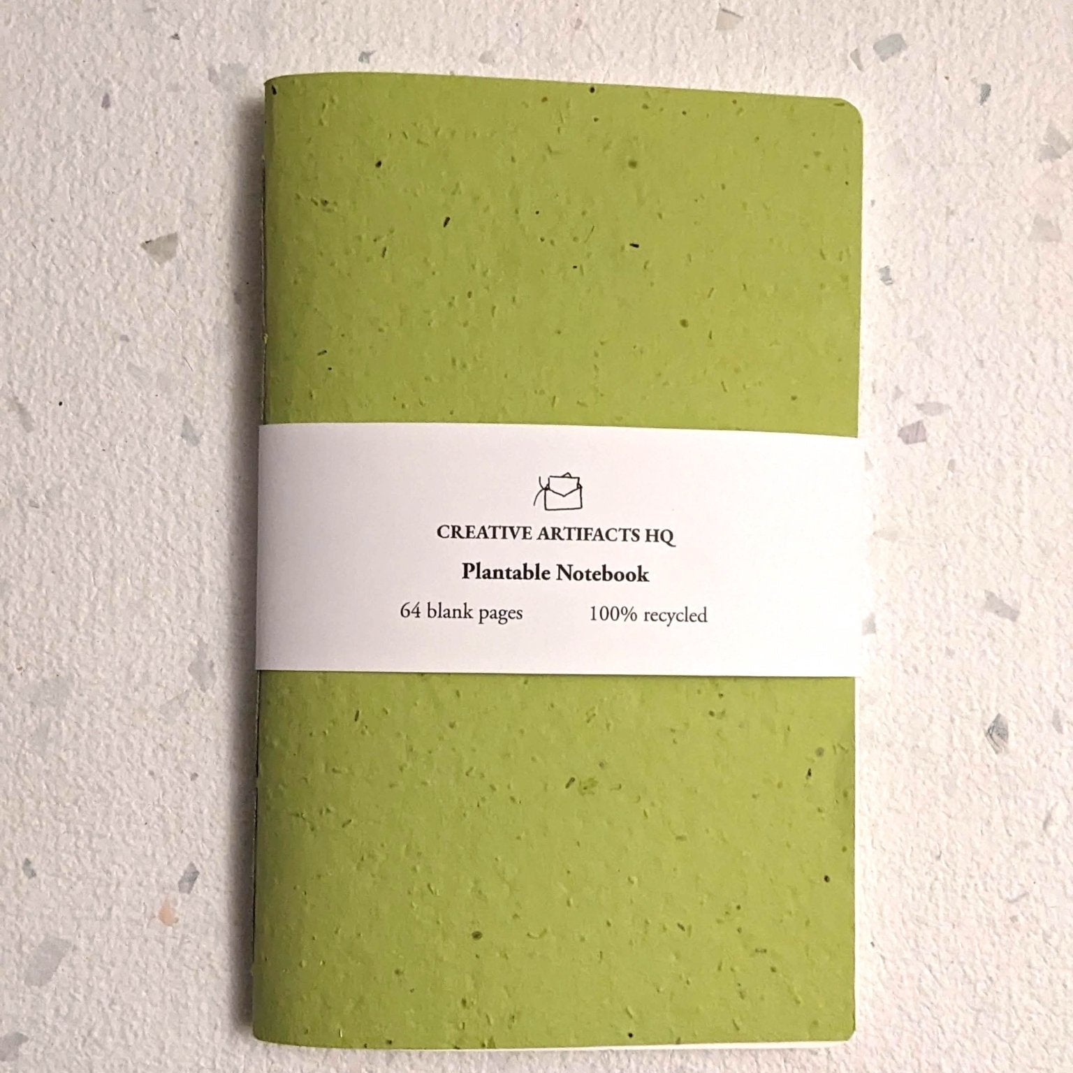 Green notebook with a white label on a textured beige background Creative Artifacts HQ plantable handmade