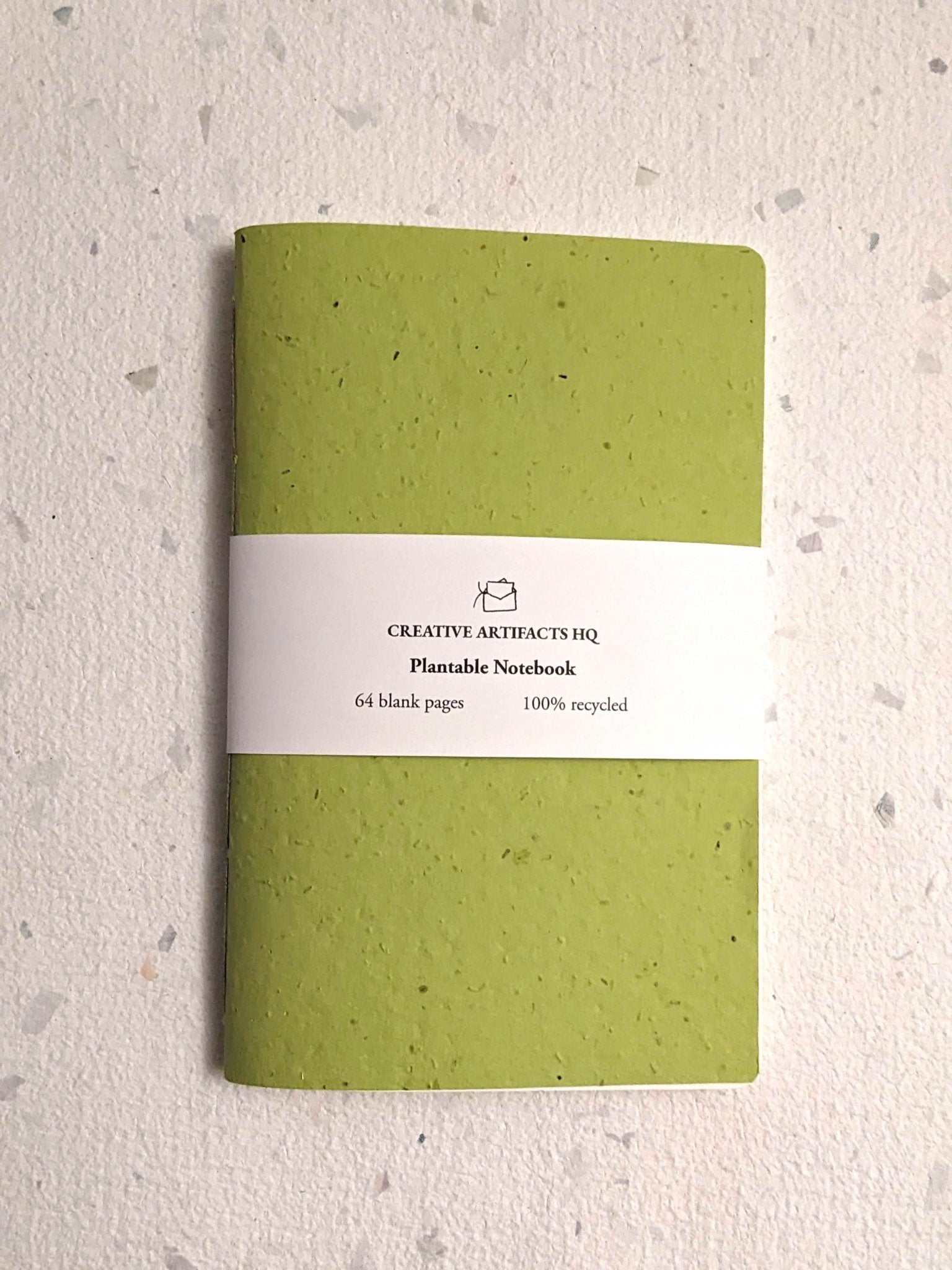 Green notebook with a white label on a textured grey surface Creative Artifacts HQ plantable 