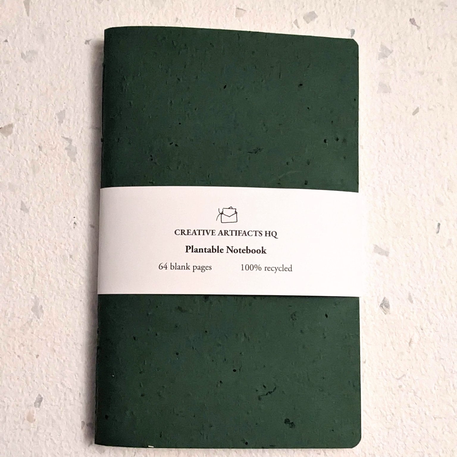 Green notebook with a label on a textured grey surface Creative Artifacts HQ plantable 