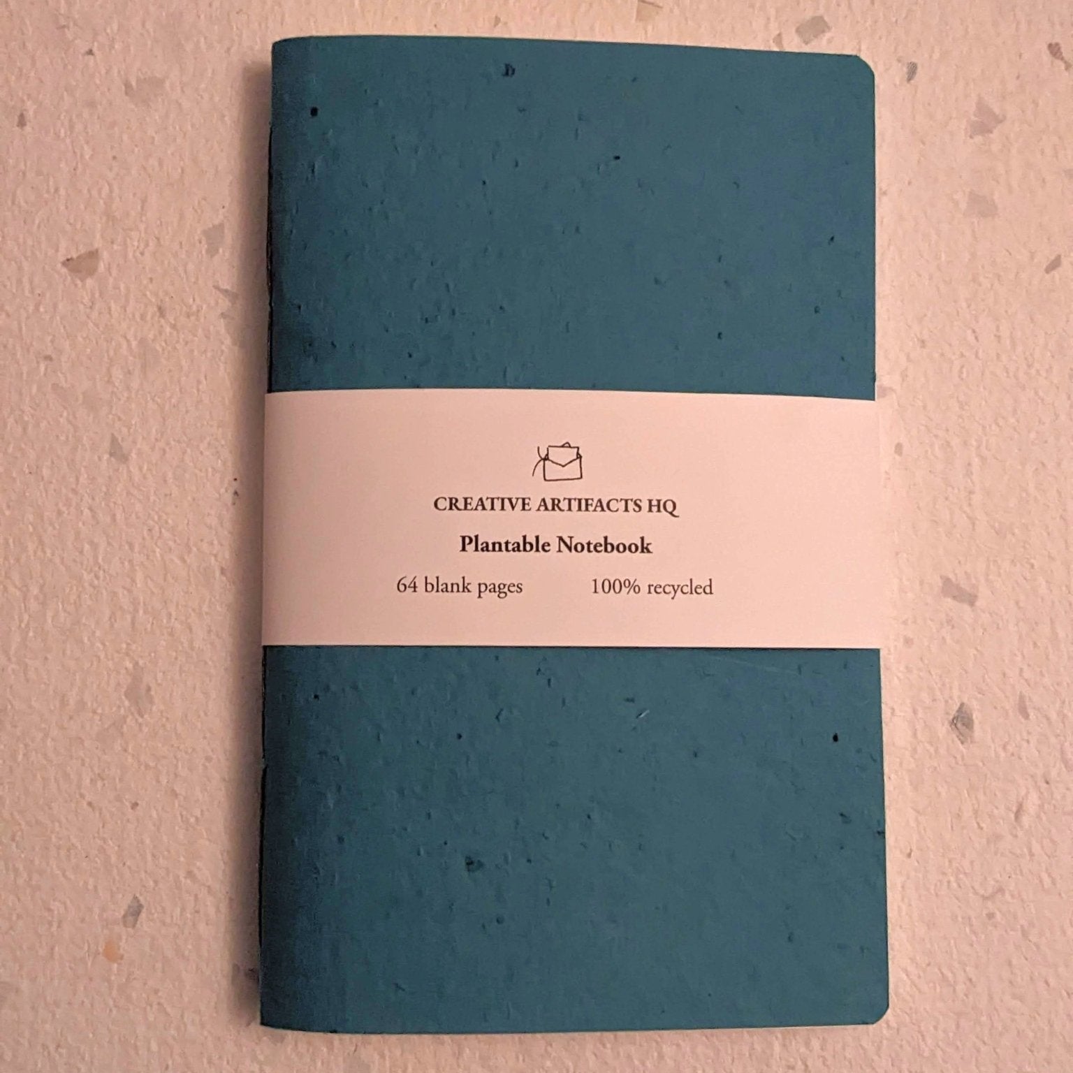 Teal notebook with a beige label on a grey surface Creative Artifacts HQ plantable 