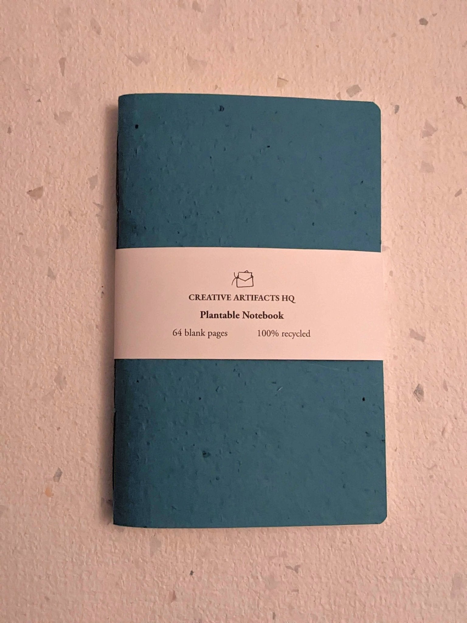 Teal notebook with a beige label on a grey surface Creative Artifacts HQ plantable 