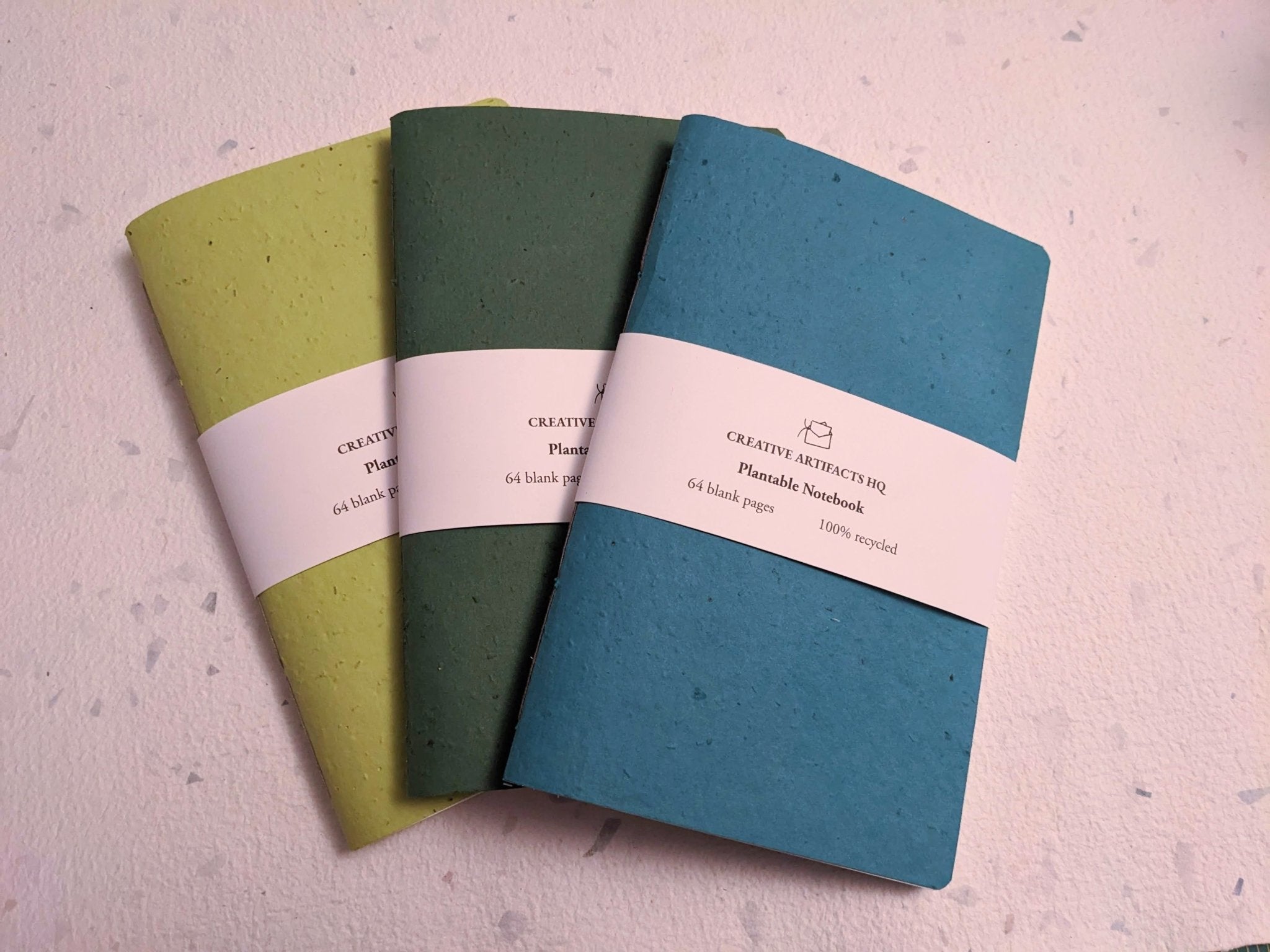 Three notebooks in green, blue, and yellow on a textured surface Creative Artifacts HQ plantable handmade