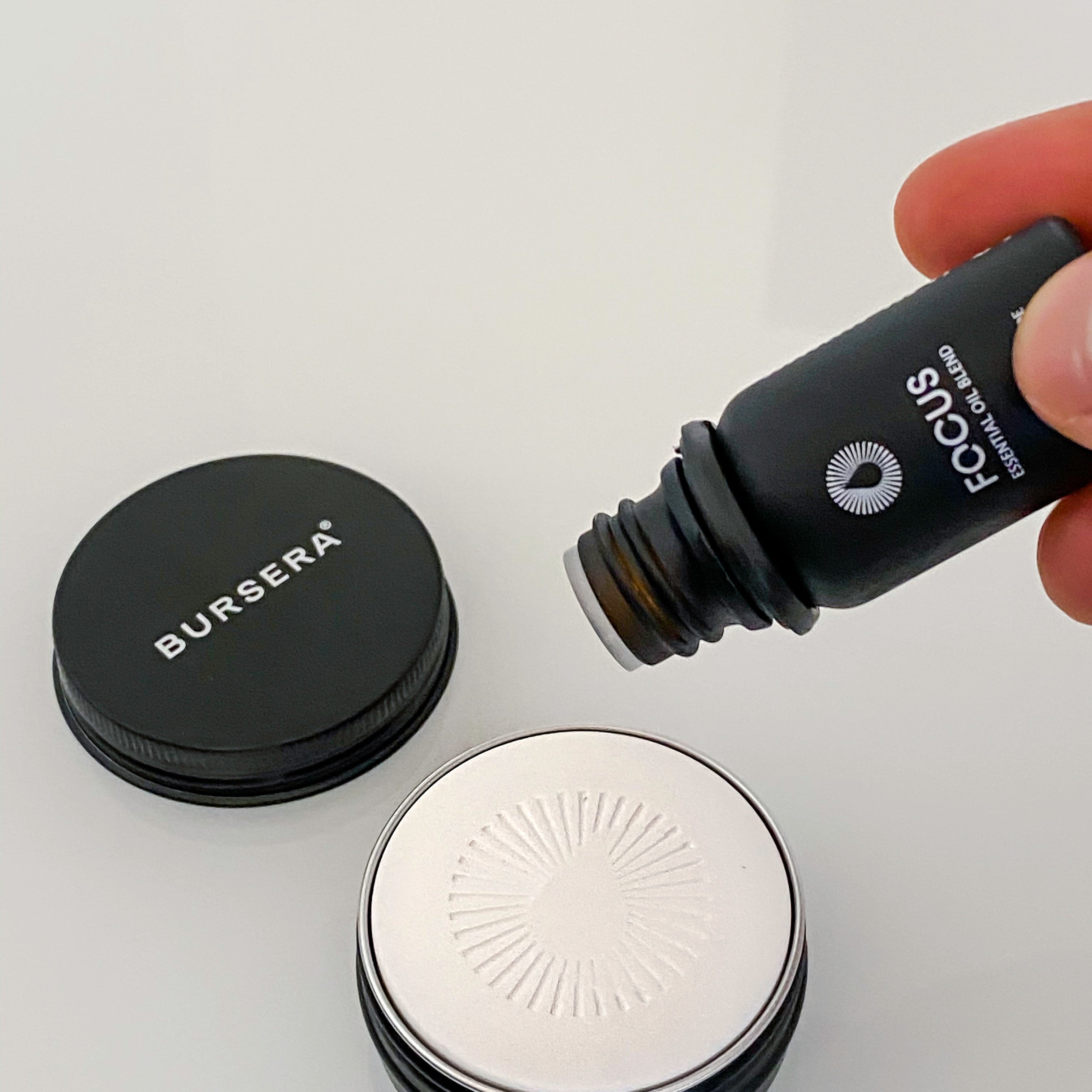 Person pouring a product from a Bursera bottle onto a white surface with a gray background