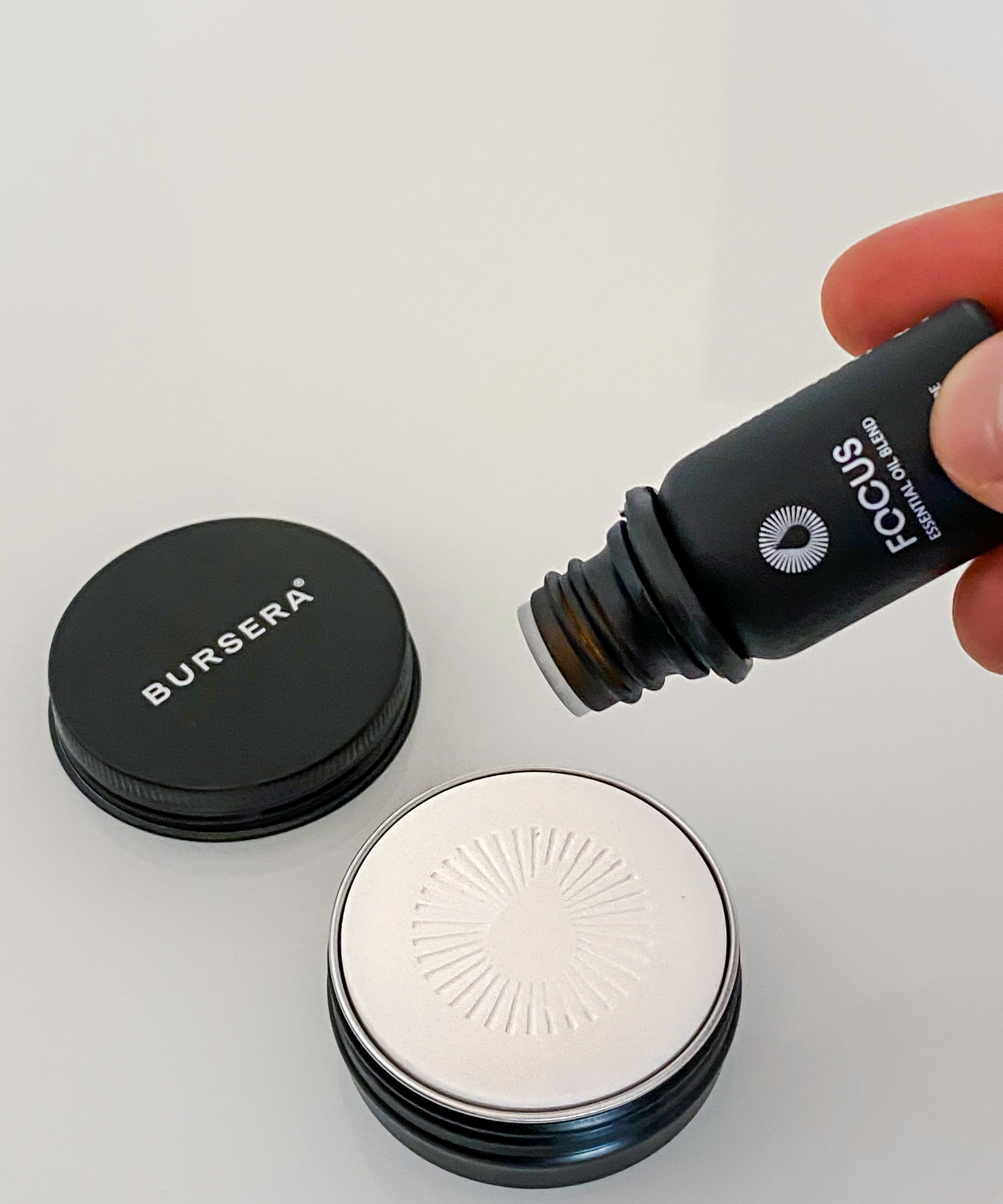 Person pouring a product from a Bursera bottle onto a white surface with a gray background