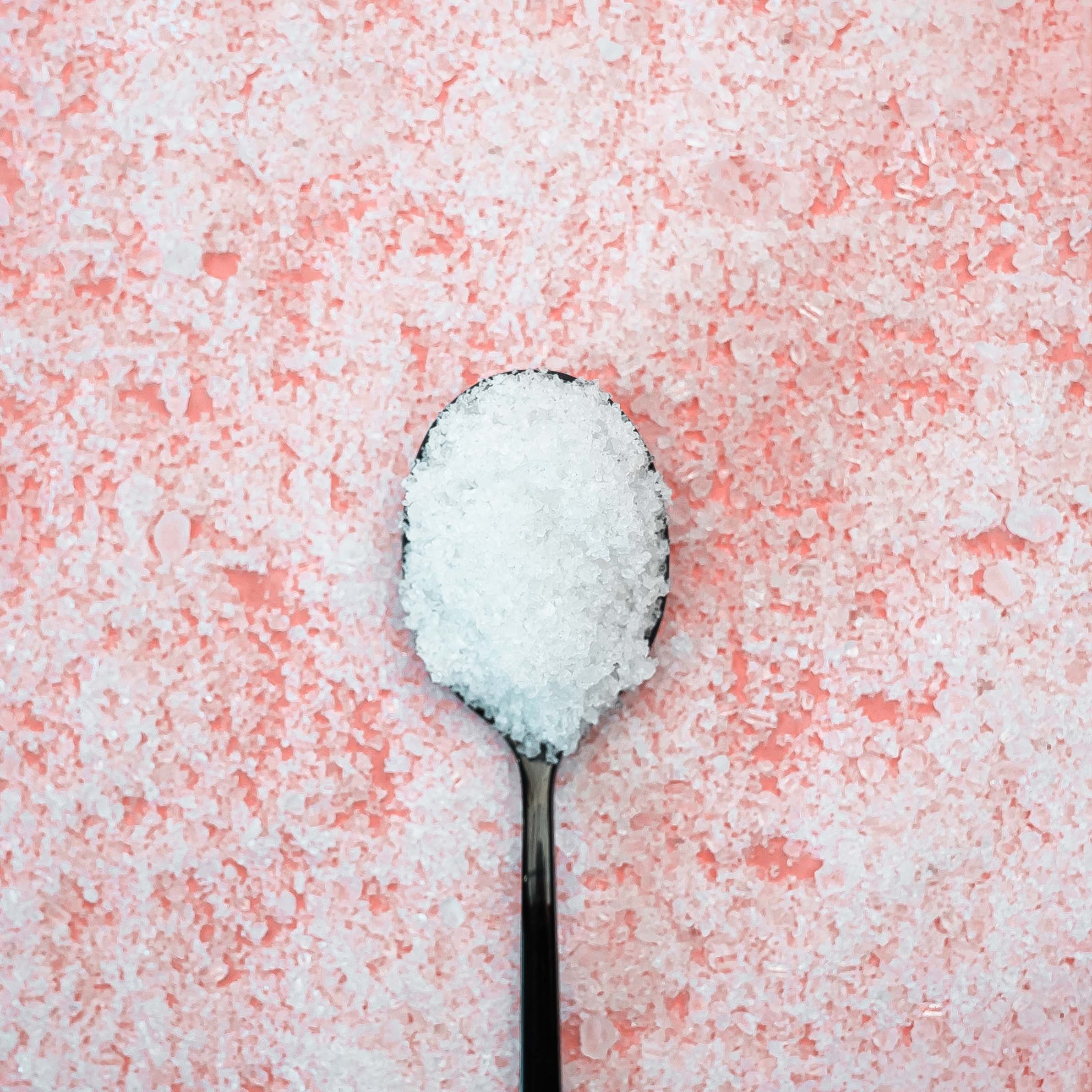 Spoon filled with white sugar on a pink sugar background