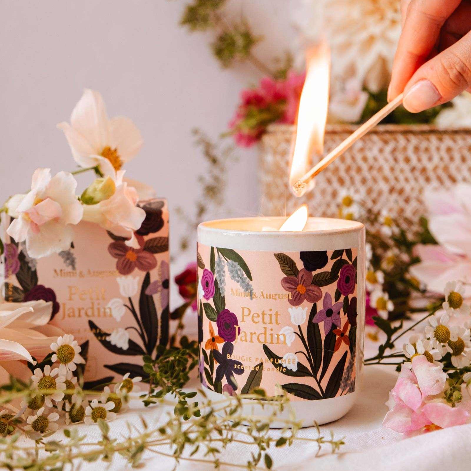 Candle being lit with floral design, surrounded by flowers and a woven basket.