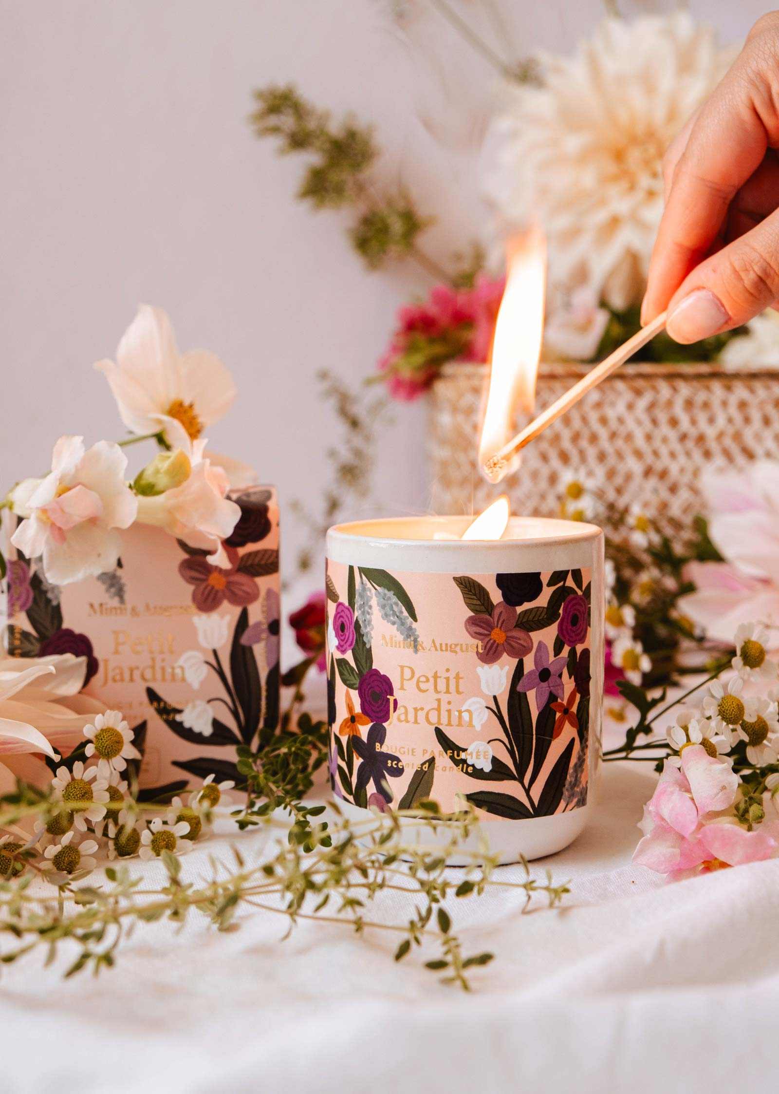 Candle being lit with floral design, surrounded by flowers and a woven basket.