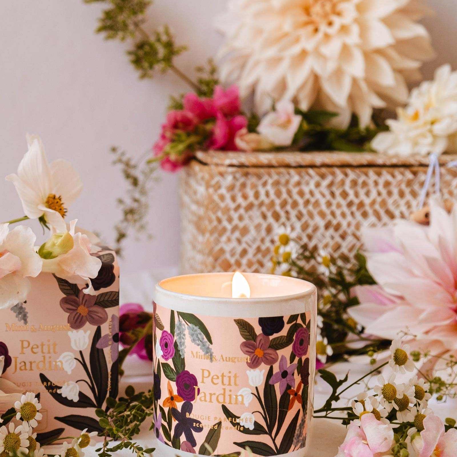 Floral-patterned candle with 'Petit Jardin' branding on a table with flowers and a white background