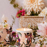 Floral-patterned candle with 'Petit Jardin' branding on a table with flowers and a white background
