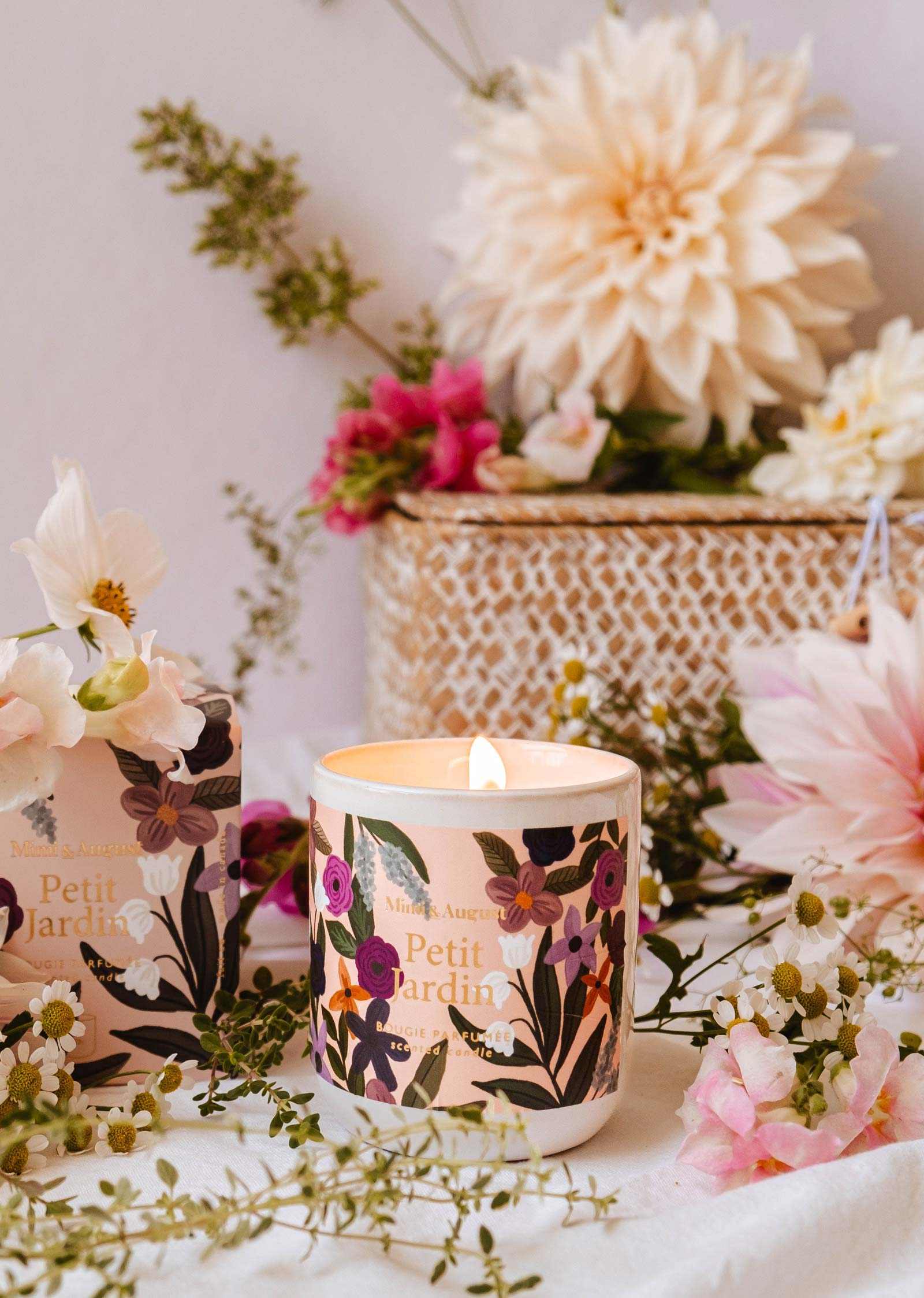 Floral-patterned candle with 'Petit Jardin' branding on a table with flowers and a white background