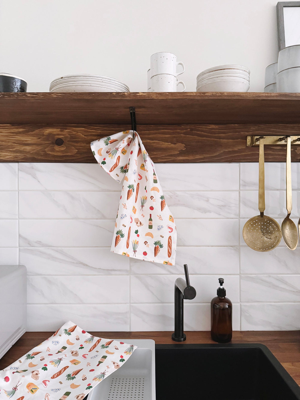 Kitchen with wooden shelf, white tiles, and a sink with a towel and bottles.