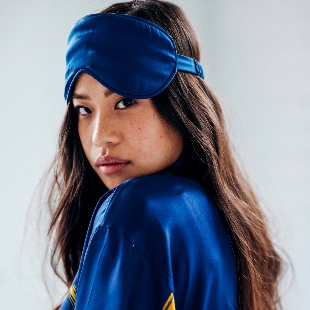 Woman wearing a blue satin eye mask and robe against a white background